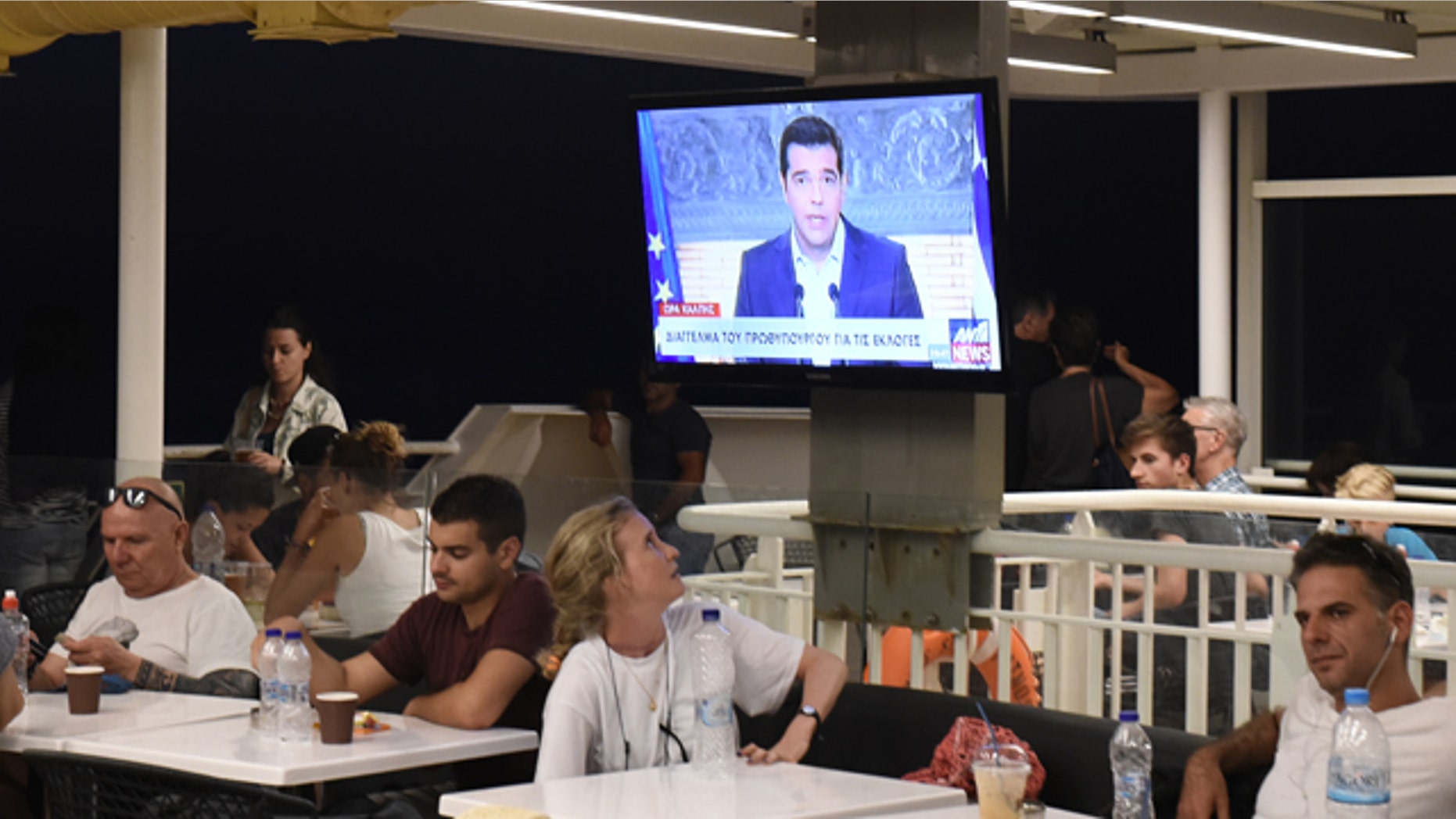 Aug. 20, 2015: A tourist watches Greek Prime Minister Alexis Tsipras, deliver a televised address to the nation, on a television screen aboard a ferry traveling in the Aegean sea, near Syros island. (AP Photo/Giannis Papanikos)