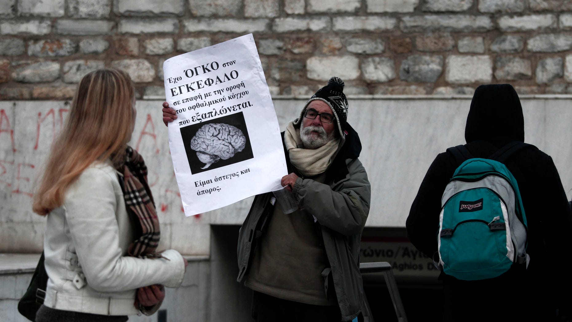 Feb. 8: Pedestrians looks on a man who holds a benner reading "I have a brain tumour - I'm jobless and homless" in the entrance of the metro station at Athens' main Syntagma square.