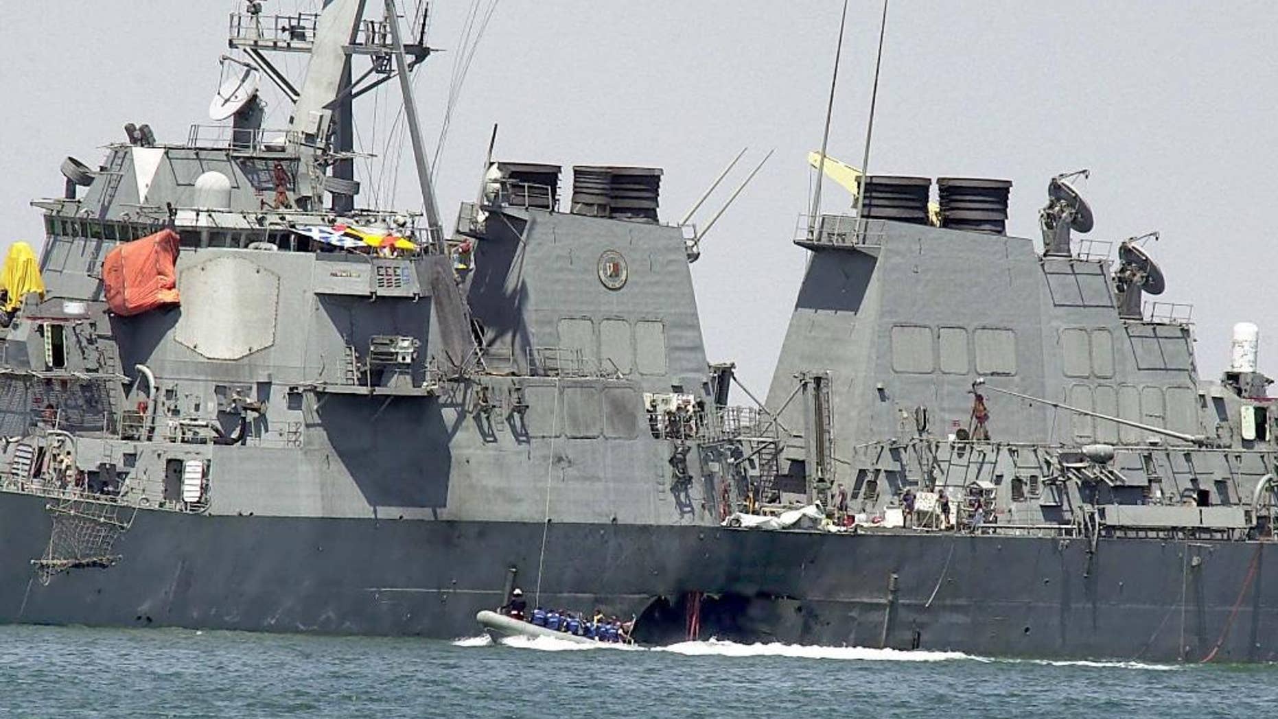 FILE -- In this Sunday Oct. 15, 2000 file photo, investigators in a speed boat examine the hull of the USS Cole at the Yemeni port of Aden, after a powerful explosion ripped a hole in the U.S Navy destroyer, killing at least 17 sailors and injuring some 30 others. Prosecutors are asking a military judge in Guantanamo Bay to reconsider his order that they share with defense attorneys details about a detainee’s experience in secret CIA prisons after he was arrested in connection with the deadly attack on the USS Cole in Yemen. (AP Photo/Dimitri Messinis, File)