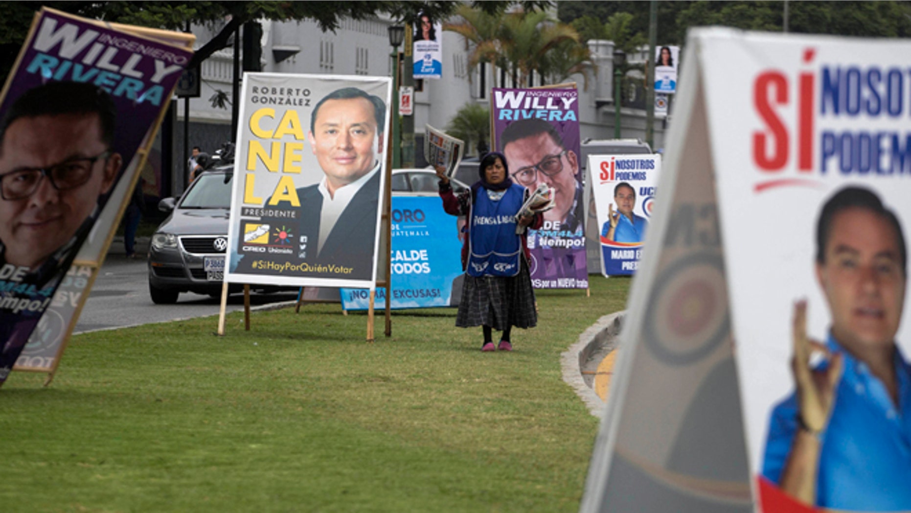 A newspaper vendor walks through a row of A-frame signs promoting presidential and mayoral candidates in Guatemala City, Thursday, July 16, 2015. A report of the United Nations International Commission Against Impunity targeting corruption in Guatemala says a percent of the money fueling its politics comes from criminal organizations, primarily drug traffickers. The report was released one day after the same commission and Guatemalan prosecutors petitioned to have a candidate for vice president stripped of his immunity for allegedly laundering funds that were later used to finance political activities. (AP Photo/Luis Soto)