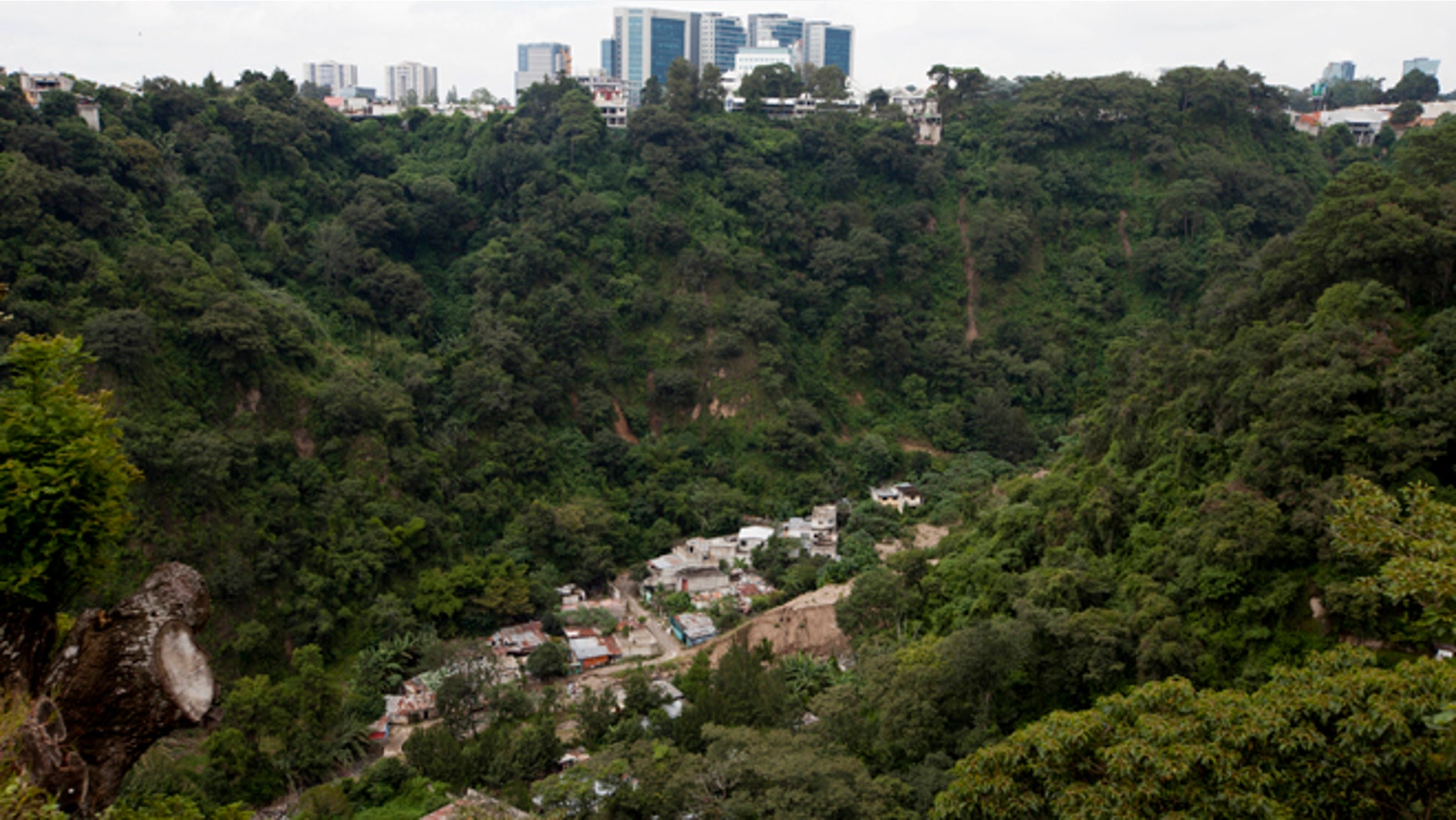 This Sept. 27, 2016 photo shows the abandoned neighborhood El Cambray, bottom, seen from the the Santa Catarina Pinula cemetery where one can also see downtown Guatemala City, one year after a mudslide unleashed at least 105 million cubic feet (3 million cubic meters) of earth on the neighborhood. The official explanation is that the river that runs along the base of the hillside had been diverted into a channel that eroded the slope. (AP Photo/Moises Castillo)
