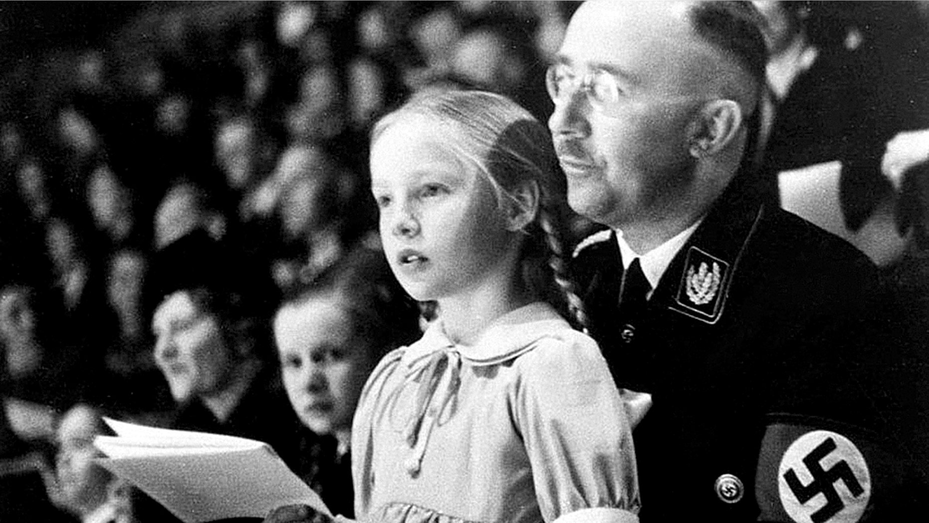 Chief of the German Police and Minister of the Interior Heinrich Himmler, with his daughter Gudrun on his lap, watch an indoor sports display in Berlin, Germany on March 6, 1938. (AP Photo)