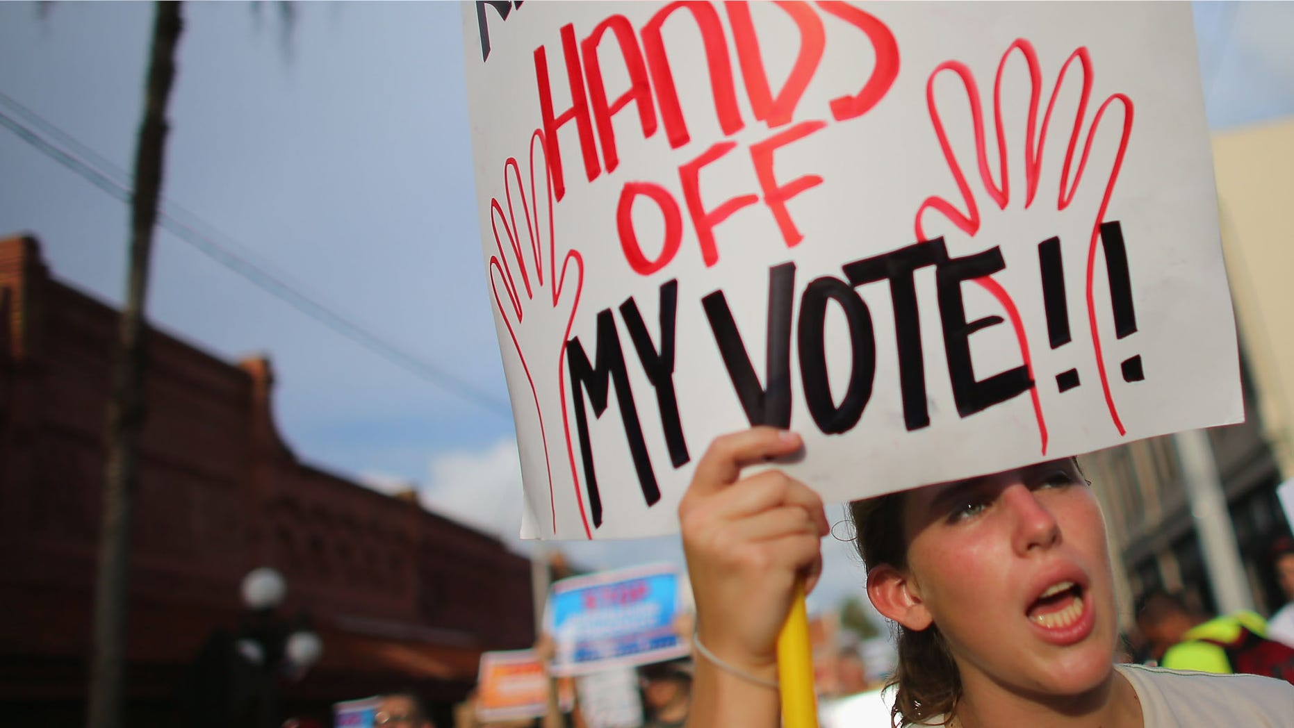 TAMPA, FL - AUGUST 28: A protester carries a sign reading, "Rick Scott, Hands off My Vote"' as she walks through the streets on the first full day of the Republican National Convention at the Tampa Bay Times Forum on August 28, 2012 in Tampa, Florida. The Republican party delegates affirmed Mitt Romney as the party's nominee as the convention began its first full session after the start was delayed due to Hurricane Isaac. (Photo by Joe Raedle/Getty Images)