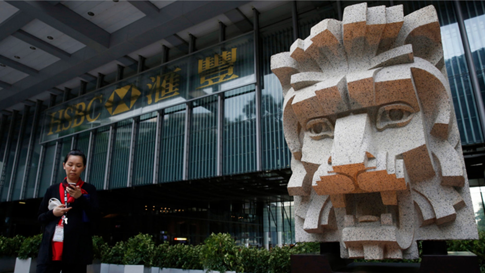 An employee of HSBC walks while checking her mobile phone in front of the HSBC building in Hong Kong Tuesday, June 9, 2015. HSBC Holdings, Britain's largest bank by market value, will cut up to 25,000 jobs around the world to reduce costs and shift its center of gravity back toward the fast-growing Asian economies where it started operations 150 years ago. Though it has not yet decided whether to move its headquarters, the bank's statement shows clearly where it thinks its commercial future lies China and the Asia-Pacific region. (AP Photo/Kin Cheung)