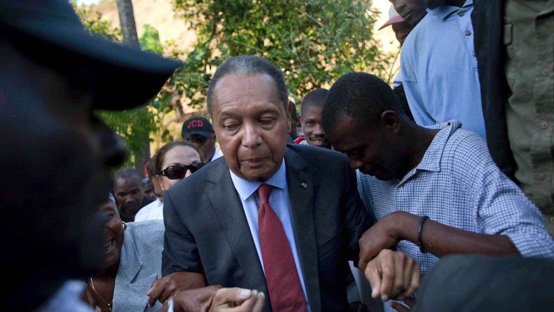 FILE - In this Feb. 8, 2011 file photo, former Haitian dictator Jean-Claude "Baby Doc" Duvalier's supporters help him negotiate an uneven path during a visit to his mother's hometown and grave site in Leogane, Haiti. Duvalier, the self-designated "president-for-life" who died Oct. 4, 2014, from an apparent heart attack, will not get a formal state funeral, but have a "simple, private,"funeral arranged by friends and family in Haiti, attorney Reynolds Georges said in an interview. (AP Photo/Ramon Espinosa, File)