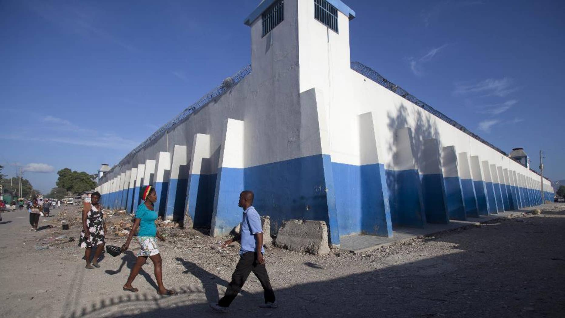 Pedestrians walk past a watch tower of the main prison in Croix-des-Bouquets, Haiti, Monday, August 11, 2014. An attack on the prison on the outskirts of the capital to free the son of a prominent businessman being held on kidnapping charges resulted in the escape of 329, officials said Monday. Police were searching throughout the country for the escaped prisoners and have also asked for help from Interpol as well as authorities in the neighboring Dominican Republic and nearby Jamaica because some of the men may have fled abroad, National Police Chief Godson Orleus said in a news conference in Port-au-Prince. (AP Photo/Dieu Nalio Chery)