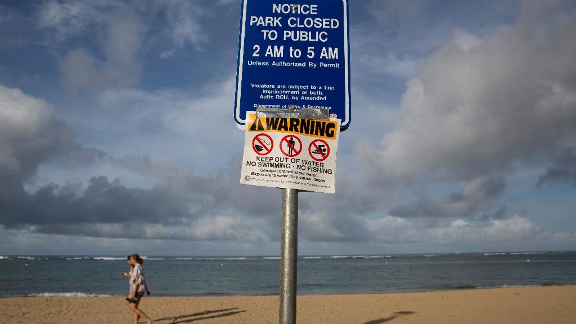 FILE - In this Aug. 25, 2015 file photo, tourists walks near a warning sign posted on Waikiki Beach in Honolulu. For the second time in a week a popular Hawaii beach was closed Thursday, Aug. 27, after sewage from a treatment plant spilled near the ocean. A million gallons of treated but not yet disinfected wastewater spilled from the East Honolulu Wastewater Treatment plant, closing Sandy Beach and its surroundings. The closure comes a day after beaches near Waikiki were reopened following a similar issue. (AP Photo/Jae C. Hong)