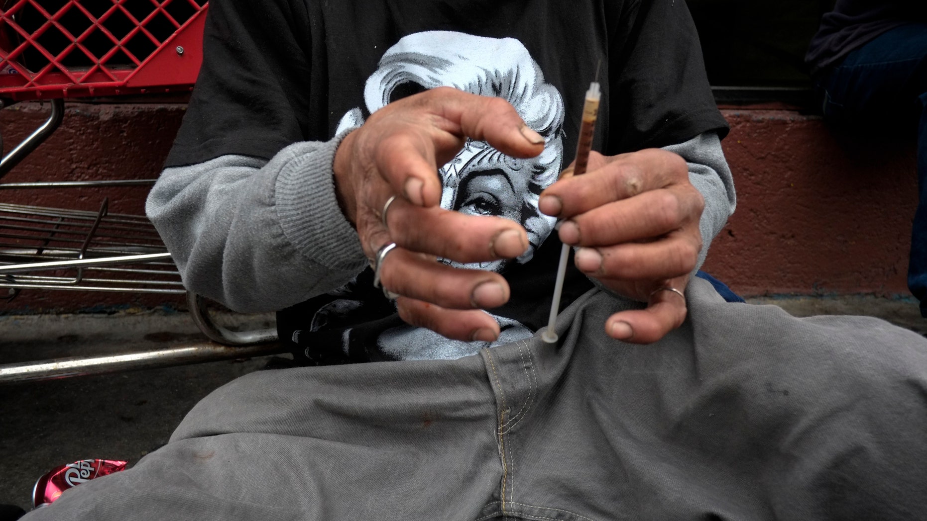 A drug addict prepares a needle to inject himself with heroin in front of a church in the Skid Row area of Los Angeles. (AP Photo/Jae C. Hong)
