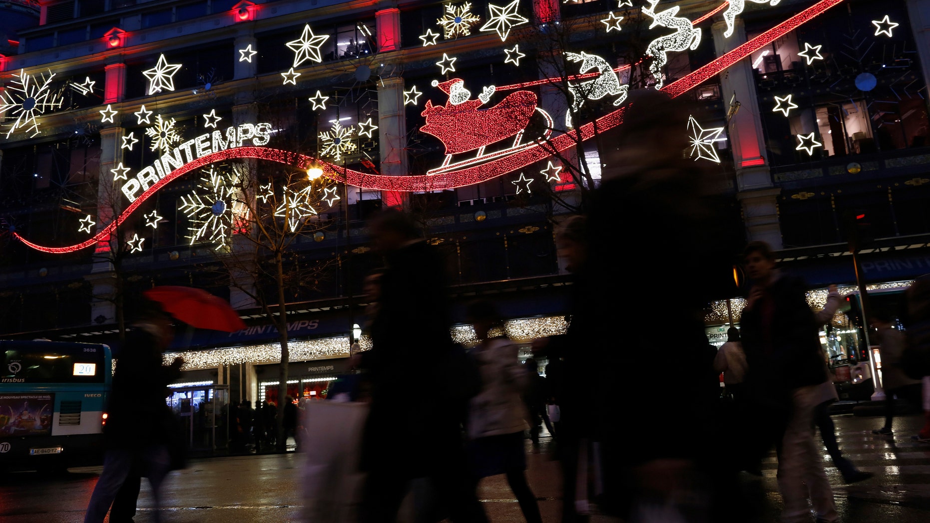 Shoppers carry bags with gifts outside a department store decorated with lights depicting Santa Claus and reindeer in Paris. Kim Komando has tips on five smartphone apps that will lead to the best deals this holiday season.