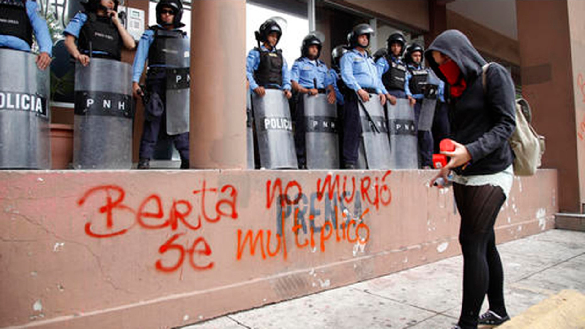 A protester writes with spray paint "Berta did not die, she multiplied" in front of riot police guarding the attorney general's office in Tegucigalpa, Honduras, Thursday, Oct. 20, 2016. Members of the Civic Council of Popular and Indigenous Organizations of Honduras (COPINH) and people belonging to the Garifuna people protested to demand justice over the March 2016 murder of Honduran indigenous leader and environmentalist Berta Caceres and to halt construction of the Agua Zarca dam, which would displace many of the indigenous Lenca people. (AP Photo/Fernando Antonio)