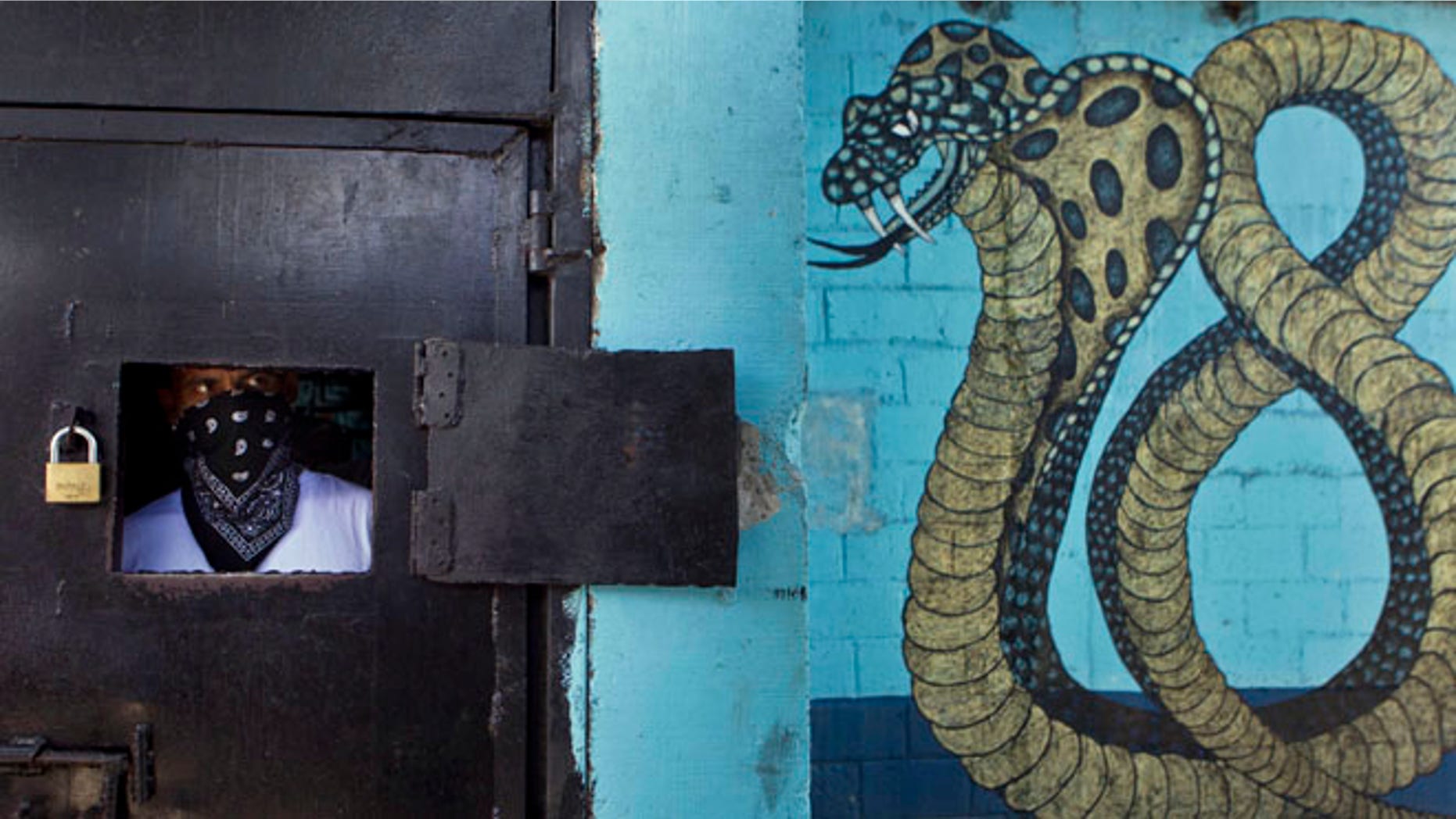 May 28, 2013: A masked member of the 18th Street gang peers from behind a window of a prison door as other gang members give a press conference inside the San Pedro Sula prison in Honduras.