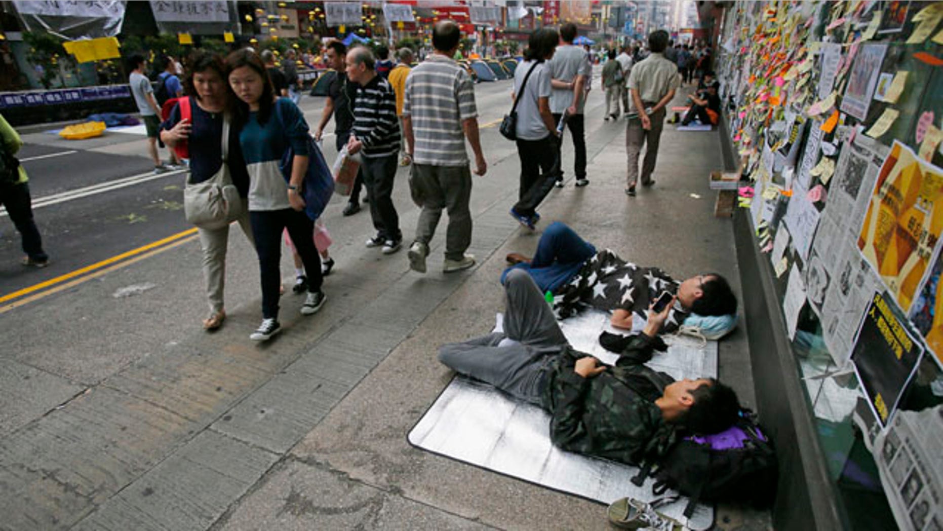 October 16, 2014: Pedestrians walk past sleeping pro-democracy students on an occupied street by the protesters in the Mong Kok district of Hong Kong. (AP Photo/Wally Santana)