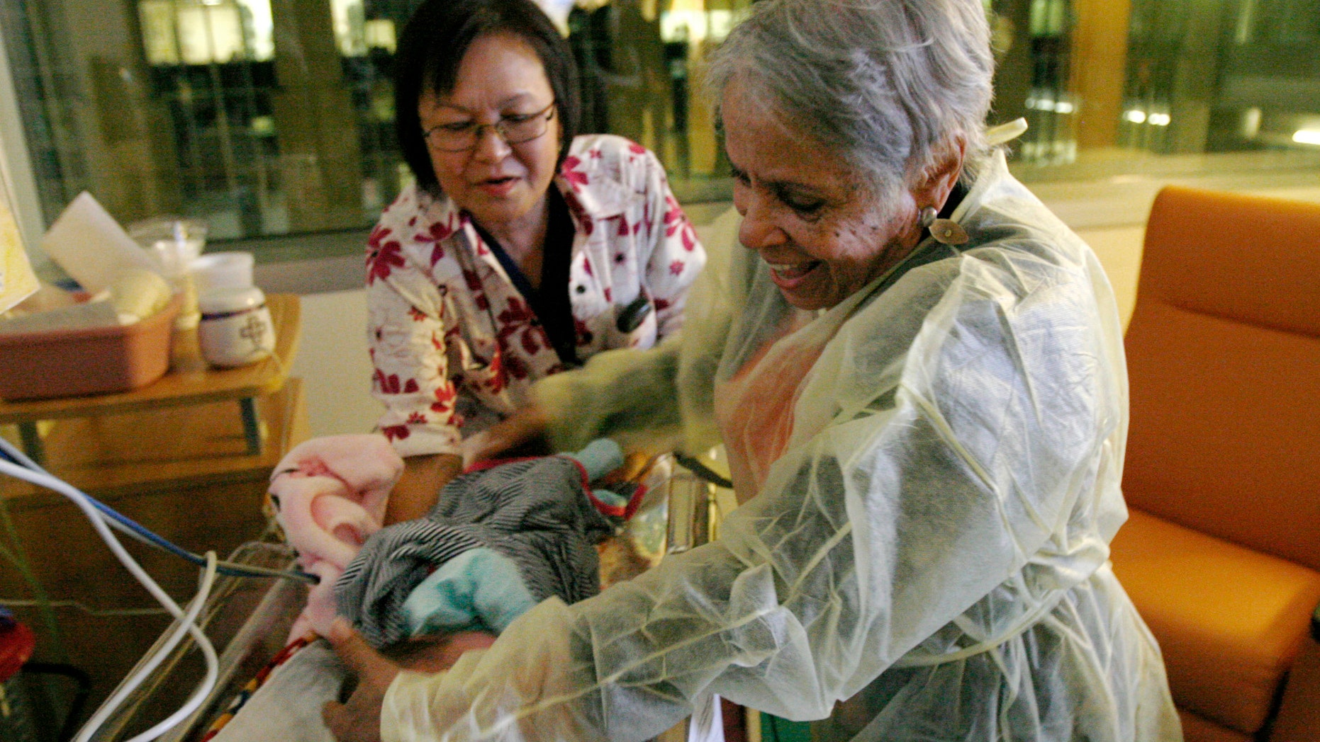 Hospital volunteer Gertie Rogers, 84, places a newborn baby back into a bed in the neonatal intensive care unit at the University of Chicago's Comer Children's Hospital in Chicago. (AP Photo/Martha Irvine)