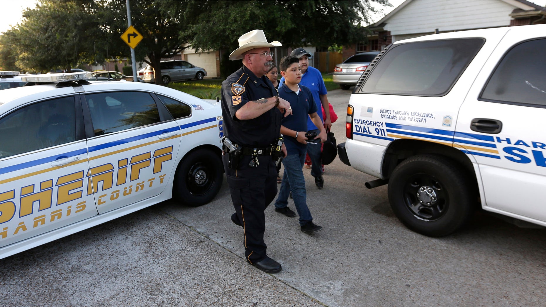 Harris County Sheriff's Department Sgt. D.J. Hilborn, left, escorts a family back to their home near the scene of a multiple shooting Sunday, Aug. 9, 2015, in Houston. Eight people, including five children and three adults, were found dead late Saturday inside a Houston-area home following the arrest of a man who exchanged gunfire with police, Texas authorities said Sunday. (AP Photo/David J. Phillip)