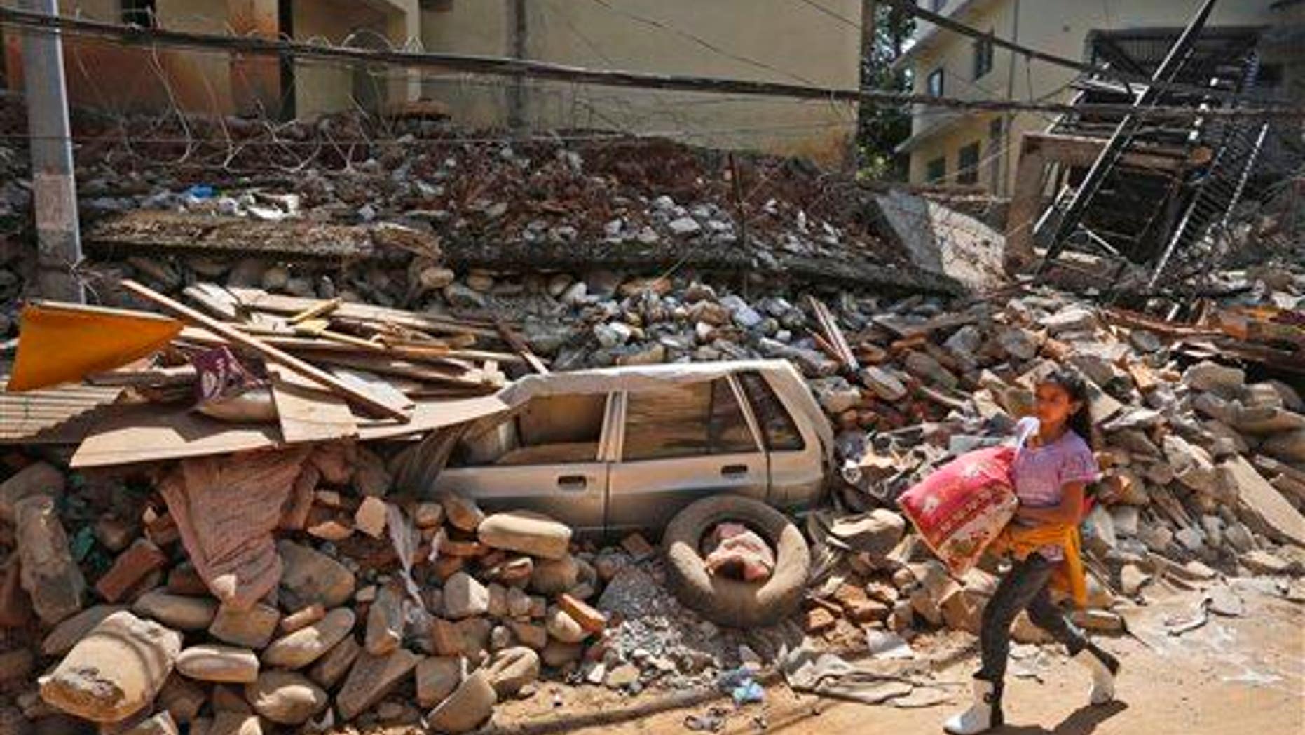A Nepalese girl walks past a car, stuck in the debris of a damaged house, carrying a quilt received as relief material in Chautara, Sindhupalchok district, Nepal, Saturday, May 2, 2015.