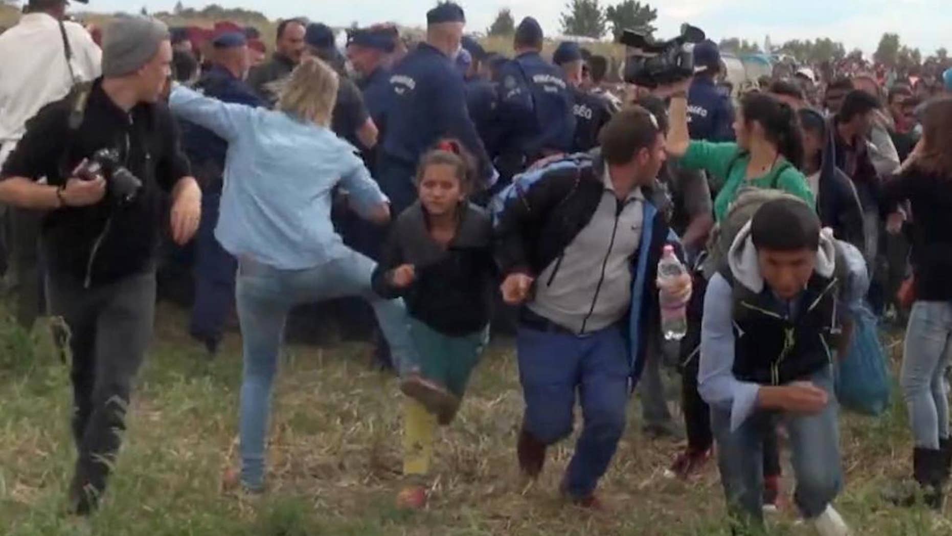 In this image taken from TV a Hungarian camerawoman, center left in blue, kicks out at a young migrant who had just crossed the border from Serbia near Roszke Hungary Tuesday Sept. 8, 2015. The camerawoman has been fired after she was caught on video kicking and tripping migrants entering Hungary across the border with Serbia. The N1TV Internet channel said their employee, widely identified in Hungarian media as Petra Laszlo, has been dismissed because she "behaved unacceptably" at a makeshift gathering point where police take migrants immediately after they enter Hungary near the village of Roszke.(Index.Hu. via AP) HUNGARY OUT