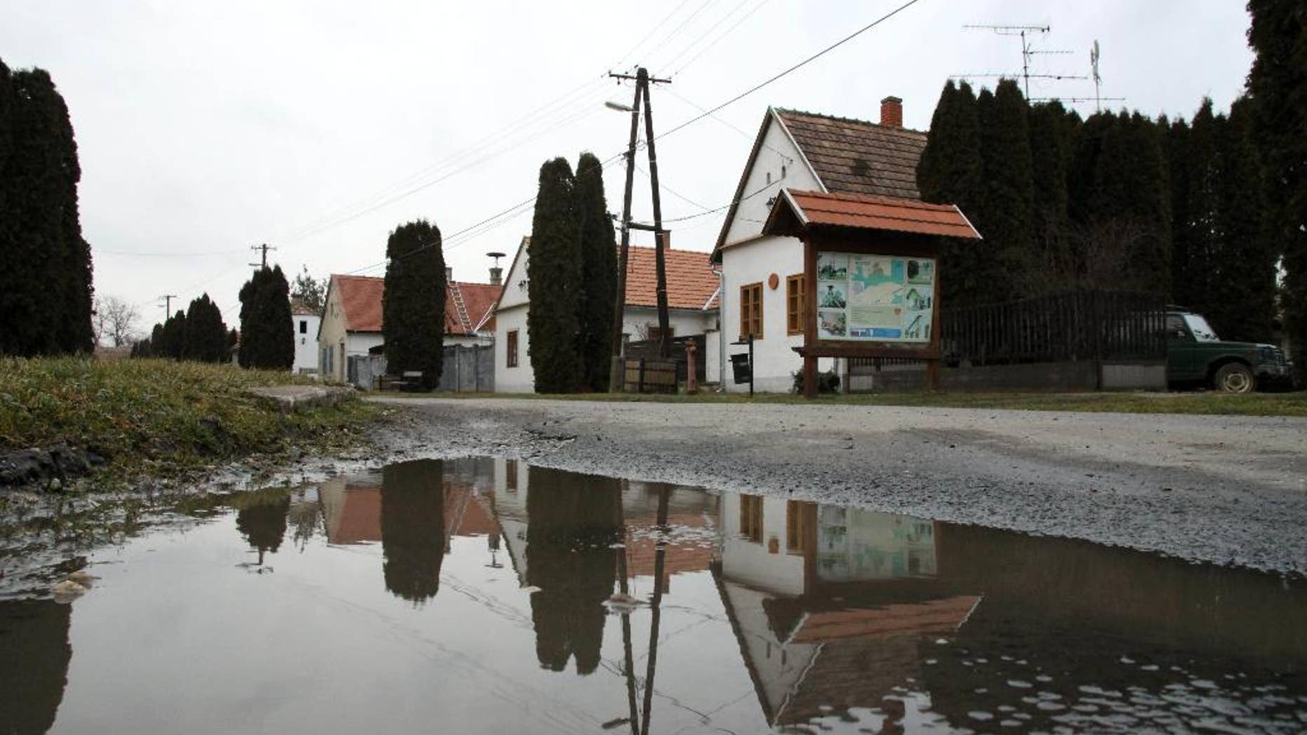 FILE - In this Wednesday, Feb. 25, 2015 file photo, houses are reflected in a puddle on the main road in the village of Megyer, Veszprem county, 190 kilometers (120 miles) southwest of Budapest, Hungary. Rooms at Hungary’s village-for-rent are going fast. Over 300 inquiries and reservations for 280 guests have been made since Mayor Kristof Pajer last week began advertising the village of Megyer, available for 210,000 forints ($760; 690 euros) a day. Pajer said Thursday, March 5, 2015, tourists are coming from as far away as Australia, South Africa, Sweden and the United States and the village “is booked solid in August and most of April and May.” (AP Photo/MTI, Lajos Nagy, File)