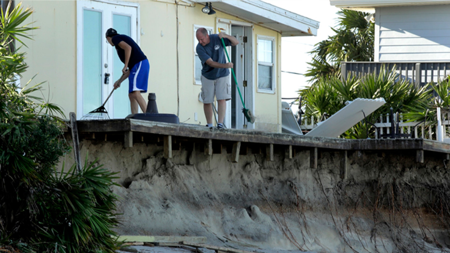 Rob Jakoby and his son Jake sweep debris off the eroded deck at his damaged beach home at Ponte Vedra Beach, Fla., Saturday, Oct. 8, 2016, after Hurricane Matthew passed through Friday. (AP Photo/Charlie Riedel)