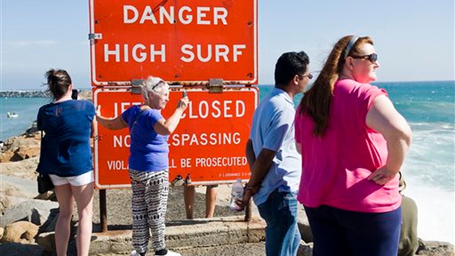 A sign warns visitors of high surf as they stand on the jetty protecting Dana Point Harbor on Saturday afternoon Sept. 6, 2014 in Dana Point, California. Hurricane Norbert in Baja California is responsible for the high surf. Norbert weakened Saturday night to a Category 1 storm with winds of up to 85 mph (140 kph). Though staying away from land, it was near enough to the coast to drench fishing villages and resorts, and pound beaches. (AP Photo/The Orange County Register, Nick Agro)