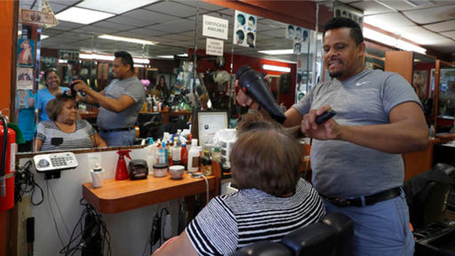 In this Wednesday, Aug. 17, 2016, photo Manolo Reyes works on a clients hair while speaking during an interview with The Associated Press in his hair salon in the Ozone Park neighborhood of the Queens borough of New York. The shooting of an imam and his assistant near their New York mosque has unnerved Muslim residents of the Ozone Park section of Queens. (AP Photo/Mary Altaffer)