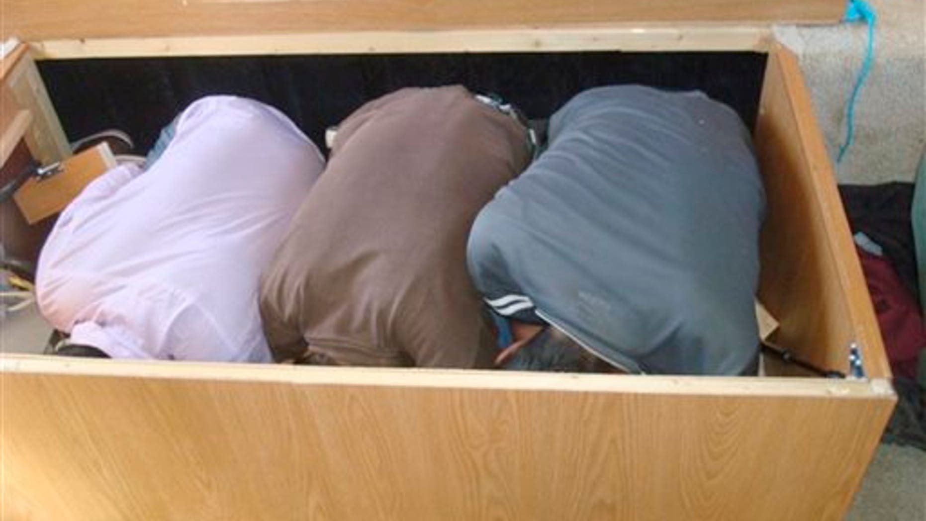This Wednesday, March 19, 2014 image provided by the U.S. Department of Homeland Security shows three adult Mexican immigrants crouched in a box after being discovered in a storage compartment under the bed of a recreational vehicle near San Diego. The vehicle's 23-year-old male driver and an 18-year-old female passenger, both U.S. citizens, were arrested on suspicion of migrant smuggling. (AP Photo/U.S. Department of Homeland Security)