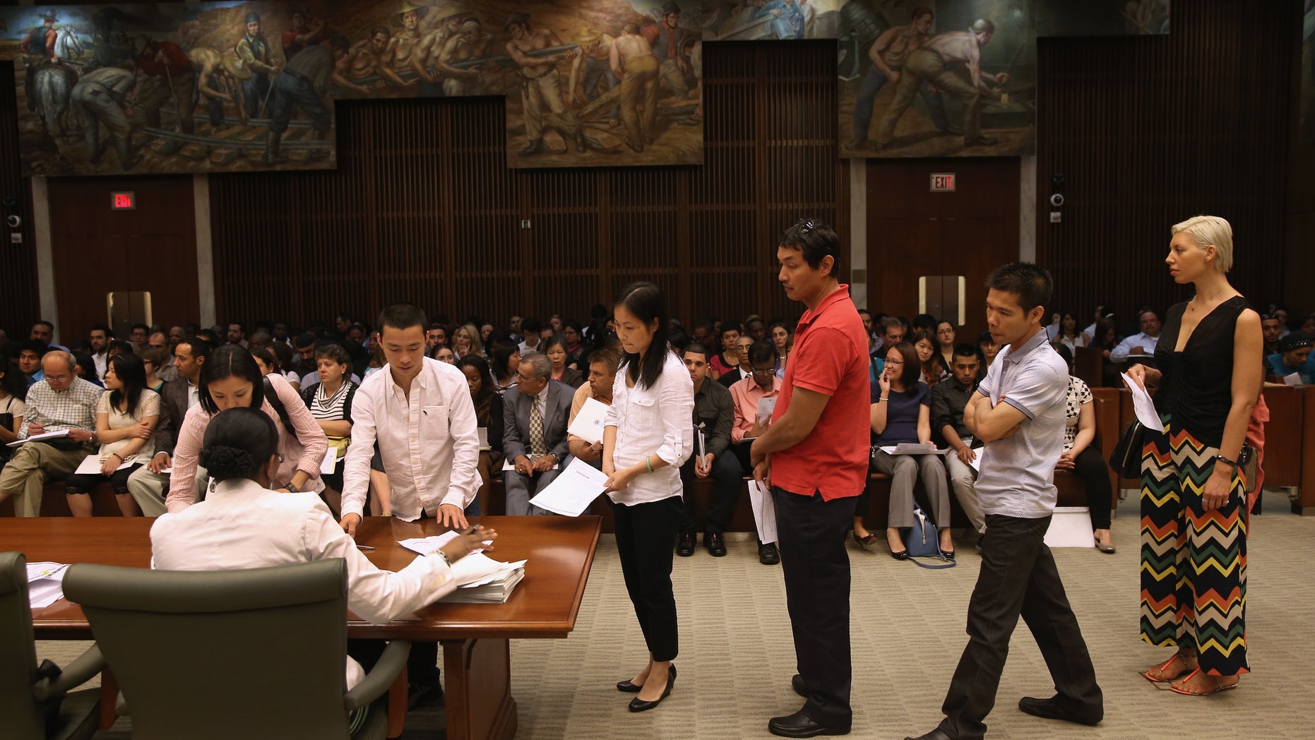NEW YORK, NY - JUNE 21: Immigrants sign their certificates of U.S. citizenship before a naturalization ceremony on June 21, 2013 in the Brooklyn borough of New York City. Some 270 people took the oath of allegiance during a ceremony held at the Theodore Roosevelt Federal Courthouse in downtown Brooklyn. One of the busiest courthouses for naturalization ceremonies in the nation, court officials say they expect to swear in some 77,000 new American citizens in Brooklyn in 2013. In the background of the courtroom hangs a 1937 Edward Laning painting "The Role of the Immigrant in the Industrial Development of America," which was salvaged from Ellis Island. (Photo by John Moore/Getty Images)