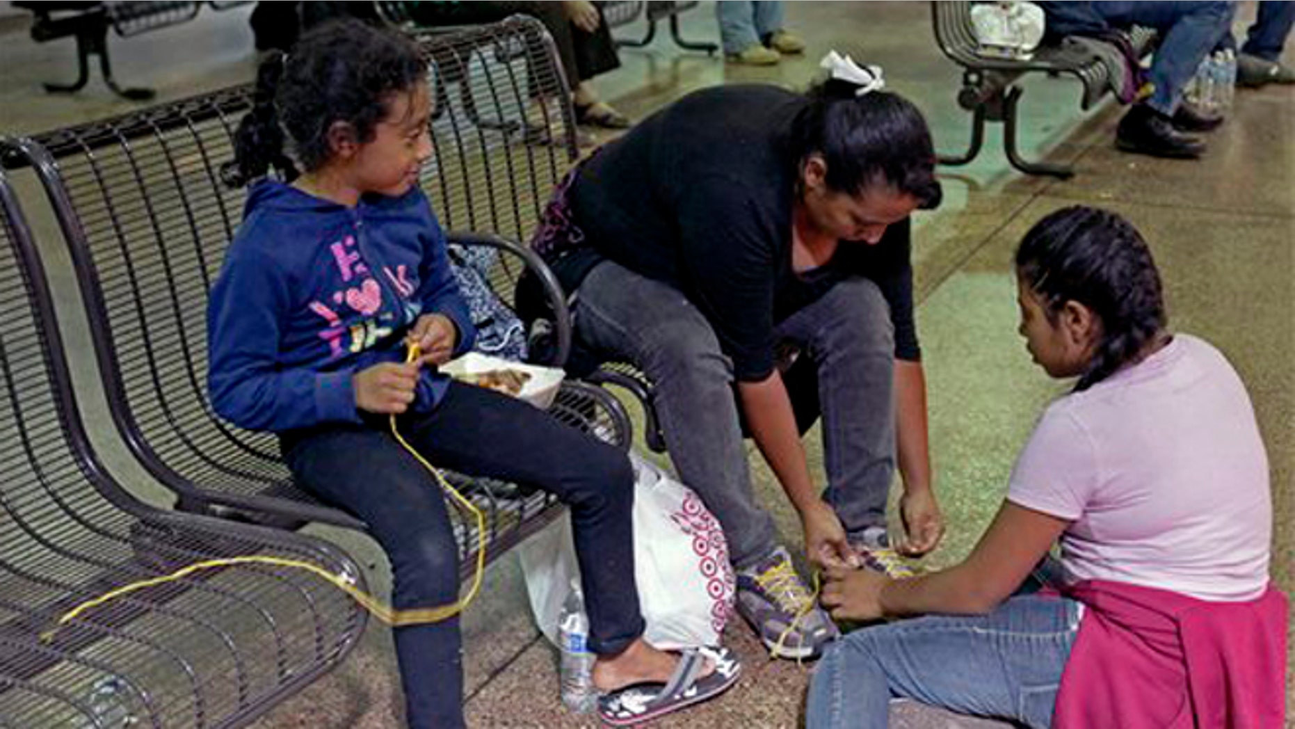Elana Carmen, middle, with her daughters Abigail, right, and Ayala, of El Salvador, tie their shoes with yellow rope for shoe laces, Thursday, May 29, 2014 at the Greyhound bus terminal in Phoenix. About 400 mostly Central American women and children caught crossing from Mexico into south Texas were flown to Arizona this weekend after border agents there ran out of space and resources. Officials then dropped hundreds of them off at Phoenix and Tucson Greyhound stations, overwhelming the stations and humanitarian groups who were trying to help. (AP Photo/Rick Scuteri)