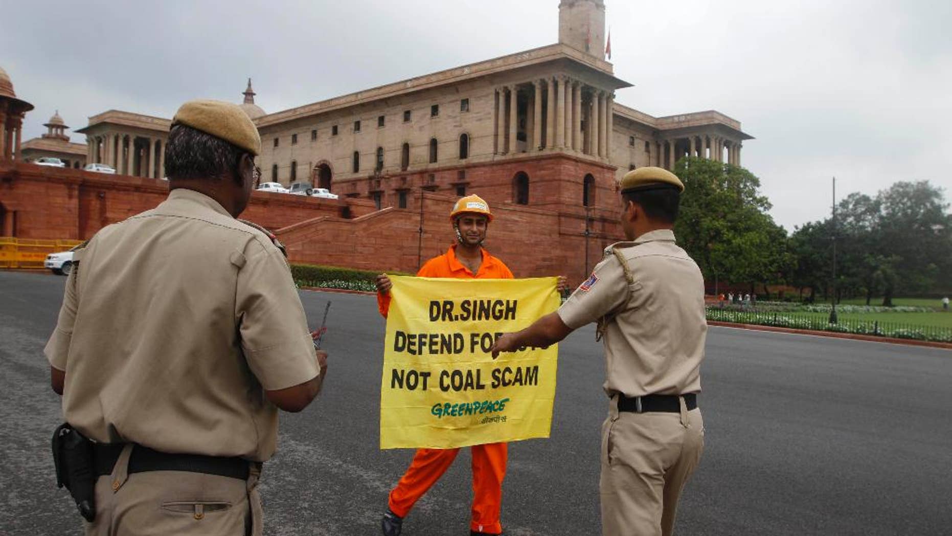 FILE- In this Aug. 21, 2012 file photo, Indian policemen prepare to remove a Greenpeace activist as he holds a banner near the area of government offices and the Indian Parliament in New Delhi, India. India's home ministry says it is temporarily suspending the registration of Greenpeace India because it is under-reporting foreign contributions and using them without government approval. (AP Photo, file)
