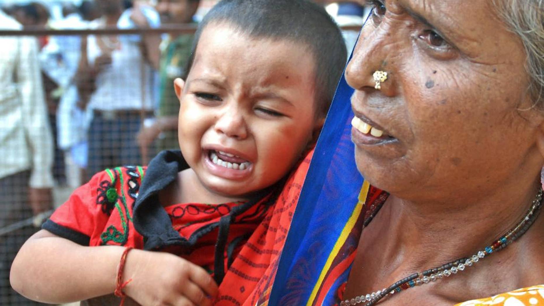 A woman holds a crying child as relatives of victims gather at the spot of a stampede at the Kamta Nath Hindu temple in Chitrakoot, India, Monday, Aug. 25, 2014. A pre-dawn stampede killed 10 people Monday as tens of thousands of Hindus were worshipping in an annual procession marking the holy day of Somvati Amavasya. (AP Photo/Amar Deep)
