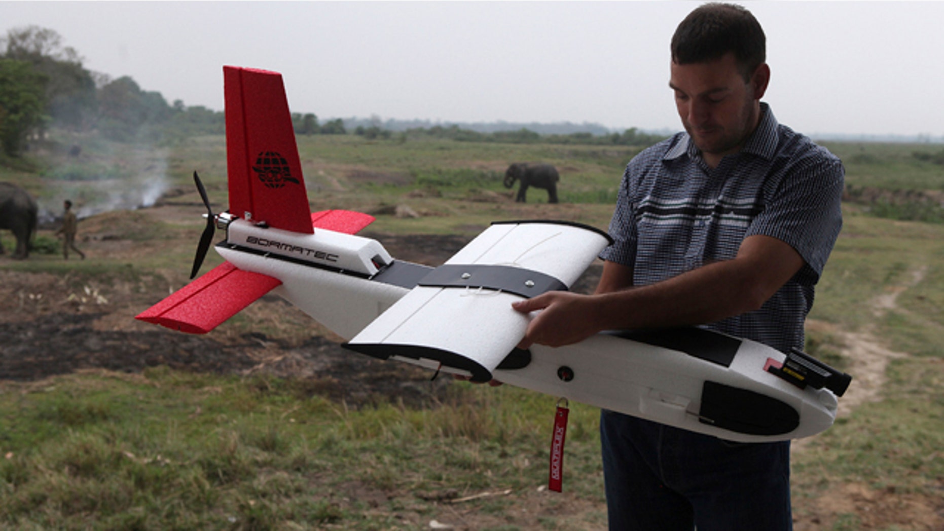 April 8, 2013: A mahout walks past with an elephant used for tourist rides as Remo Peduzzi, Managing Director, Research Drones LLC Switzerland prepares to fly an unmanned aircraft or drone at the Kaziranga National Park at Kaziranga in Assam state, India.