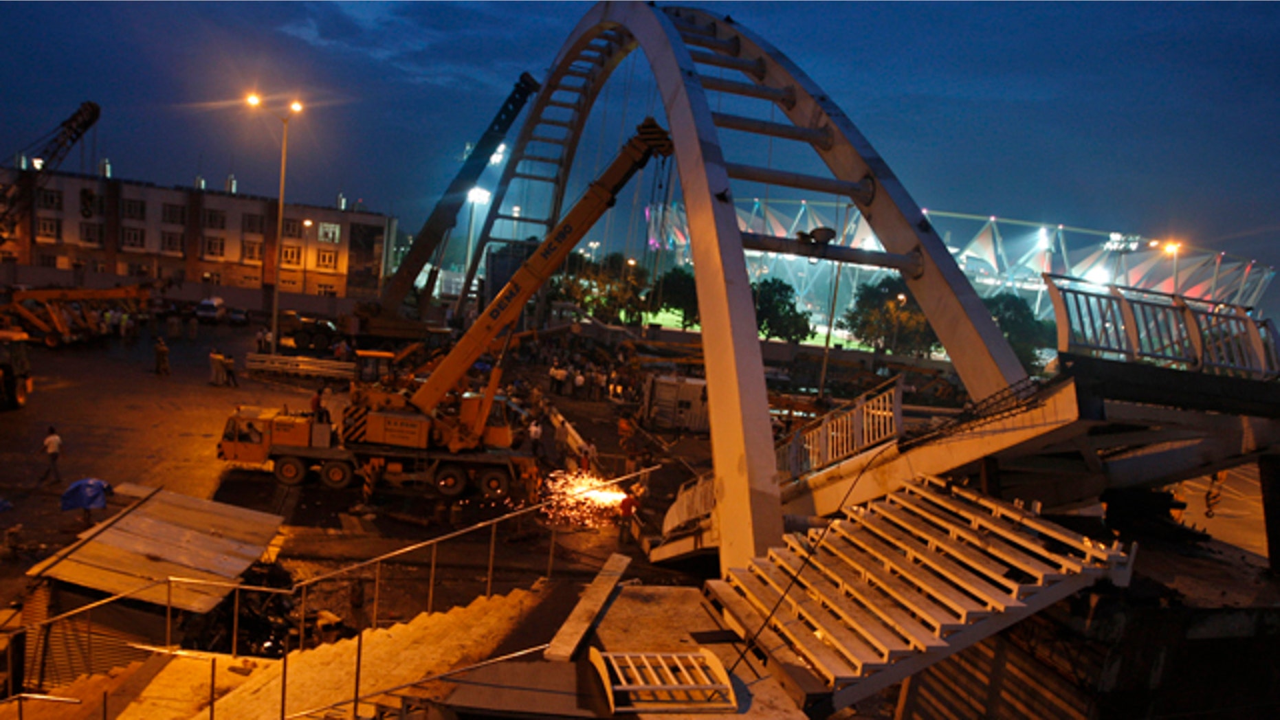 September 21: Indian workers remove debris from a collapsed bridge near an illuminated Jawaharlal Nehru stadium in New Delhi, India. A footbridge under construction near the Commonwealth Games main stadium collapsed on Tuesday, injuring people, police said. The games are scheduled to be held from Oct. 3-14. (AP)