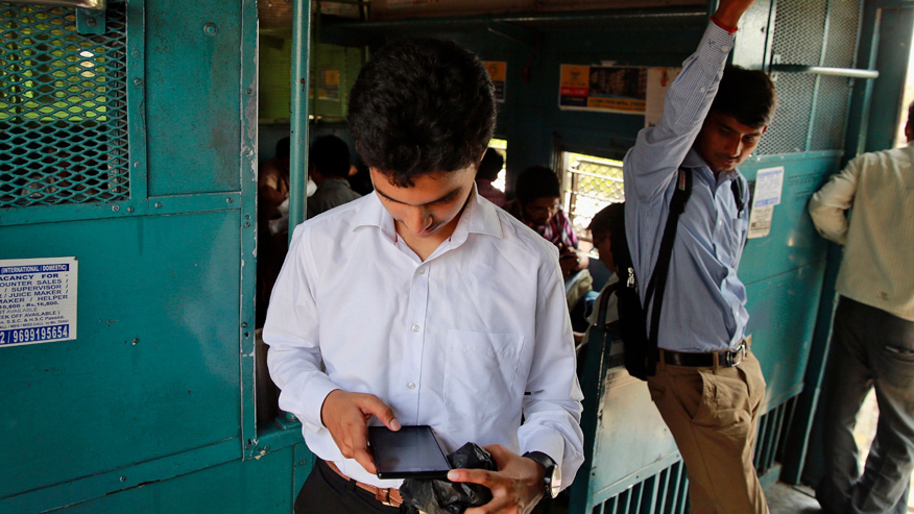 An Indian man surfs the internet on his smartphone as he travels in a local train in Mumbai, India, Tuesday, March 24, 2015.