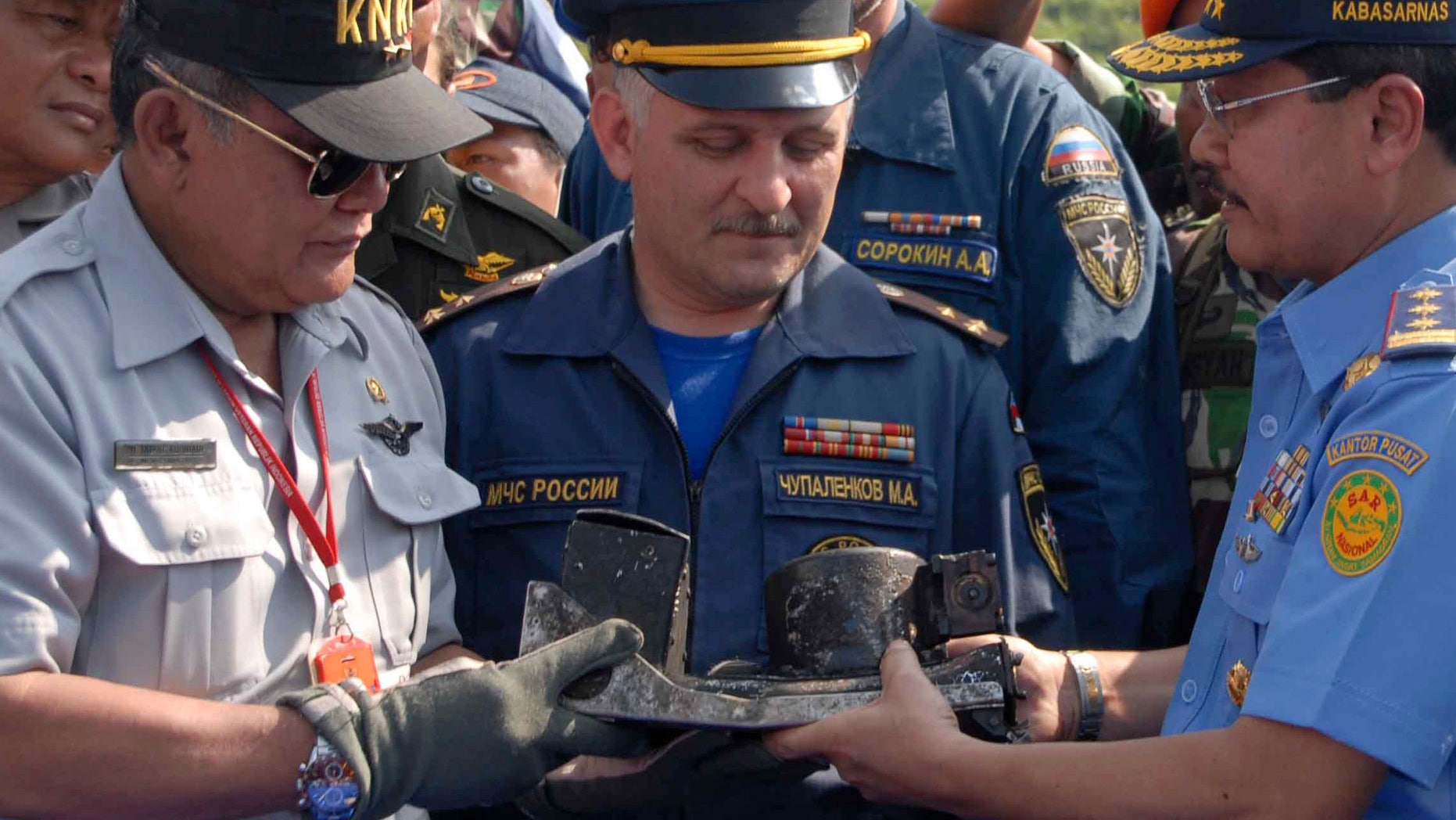 May 16, 2012: Chief of Indonesian National Transportation Safety Board Tatang Kurniadi, left, National Search and Rescue Agency head Daryatmo, right, and an unidentified Russian investigator inspect the burnt cockpit voice recorder of a Sukhoi Superjet-100.
