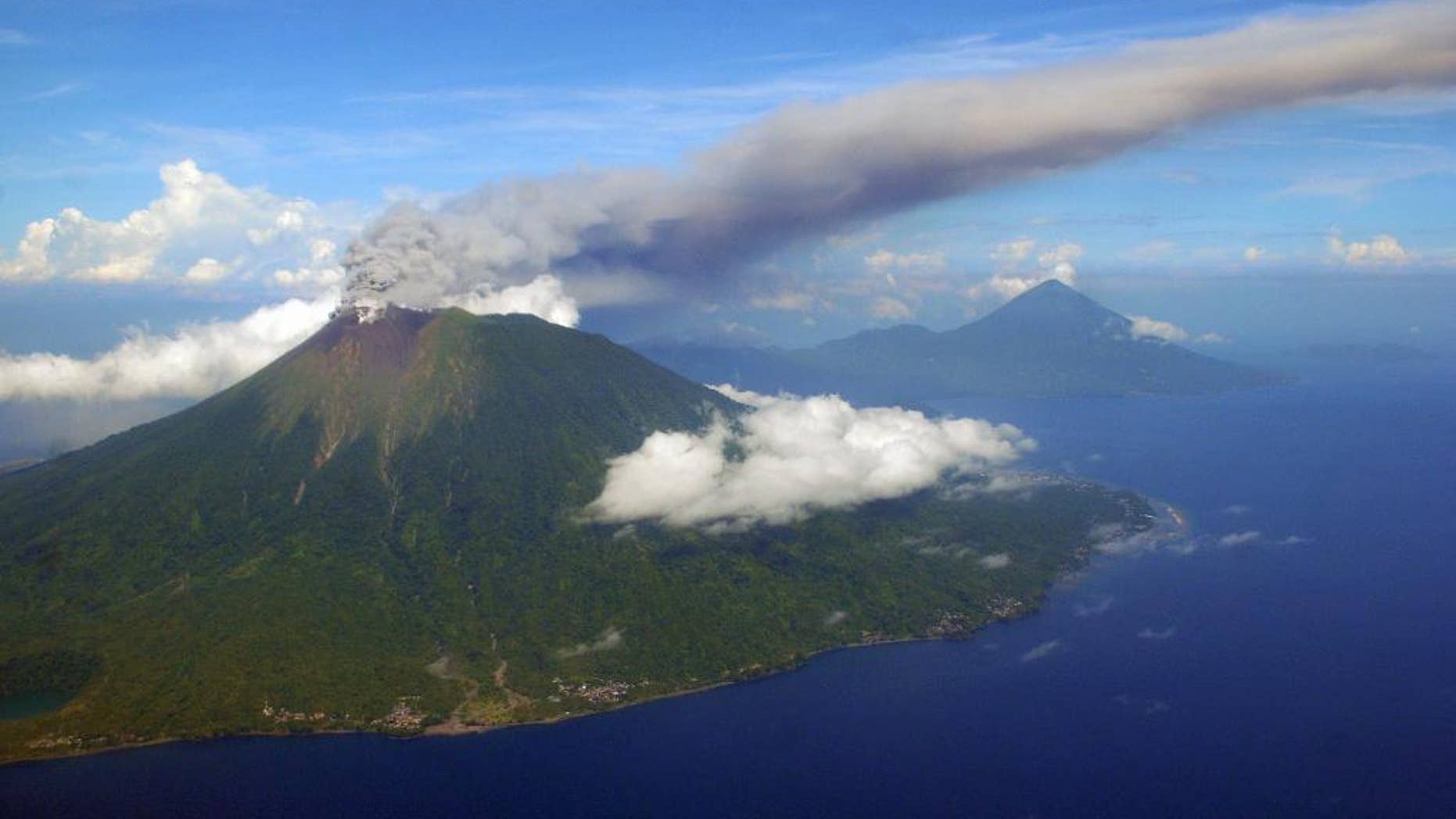 FILE - In this Sept. 16, 2012 file aerial photo taken through a passenger jet glass window, Mount Gamalama spews volcanic ash as it erupts on Ternate Island, eastern Indonesia. The volcano in North Maluku province erupted Friday, Dec. 19, 2014, spewing towering clouds of hot ash into the air and leaving four hikers injured and one missing when they scrambled to safety, an official said. (AP Photo/File)