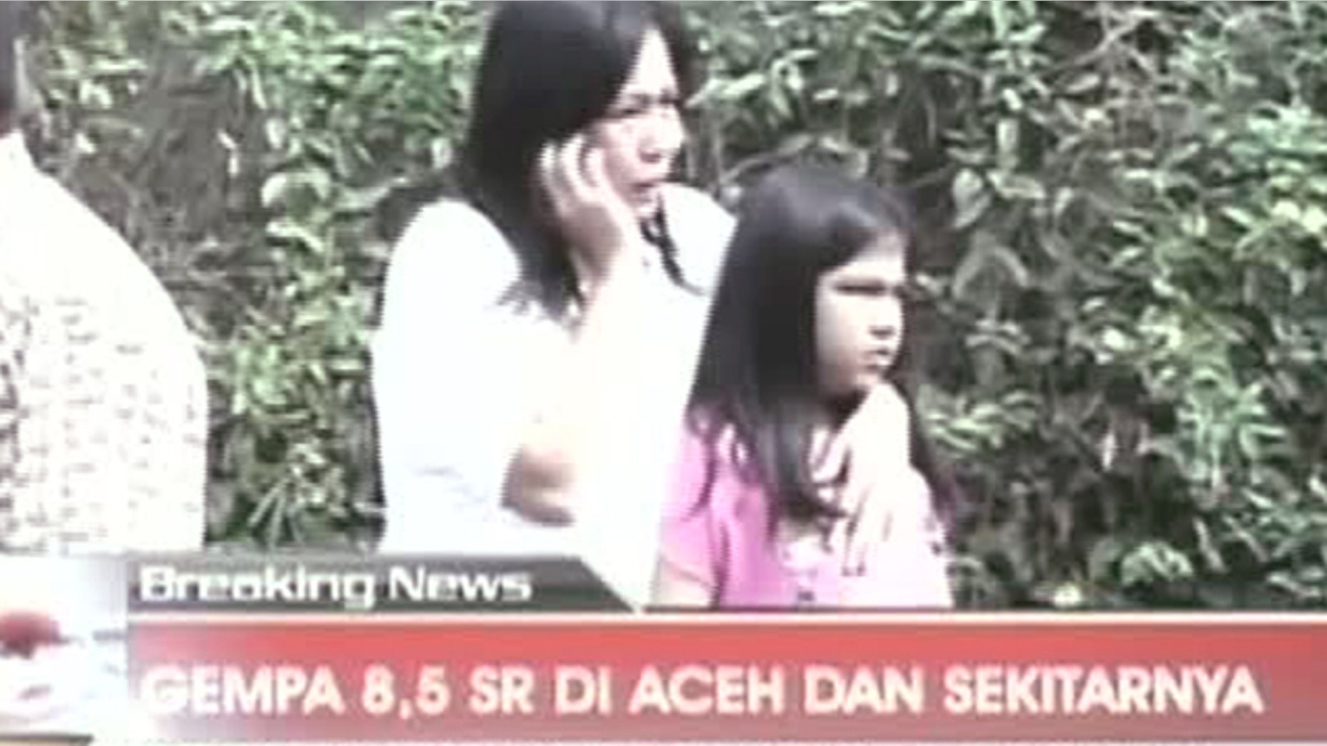 April 11, 2012: In this image made from Indonesian television TV One, a woman hugging a girl uses a mobile phone shortly after they ran out from a building when a strong earthquake hit in Aceh in Indonesia.