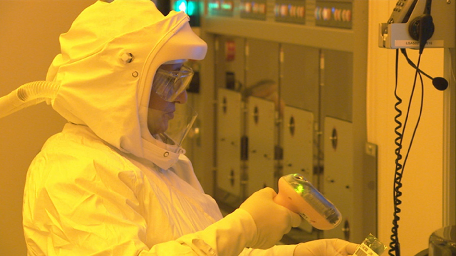 A manufacturing technician, wearing a protective suit to keep dust particles out of a clean room, uses a scanner to start production of CPU wafers inside an Intel chip factory in Chandler, Ariz.