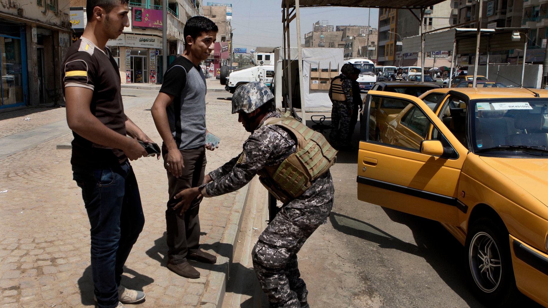 July 15, 2012: An Iraqi police officer searches people at a checkpoint in central Baghdad, Iraq.