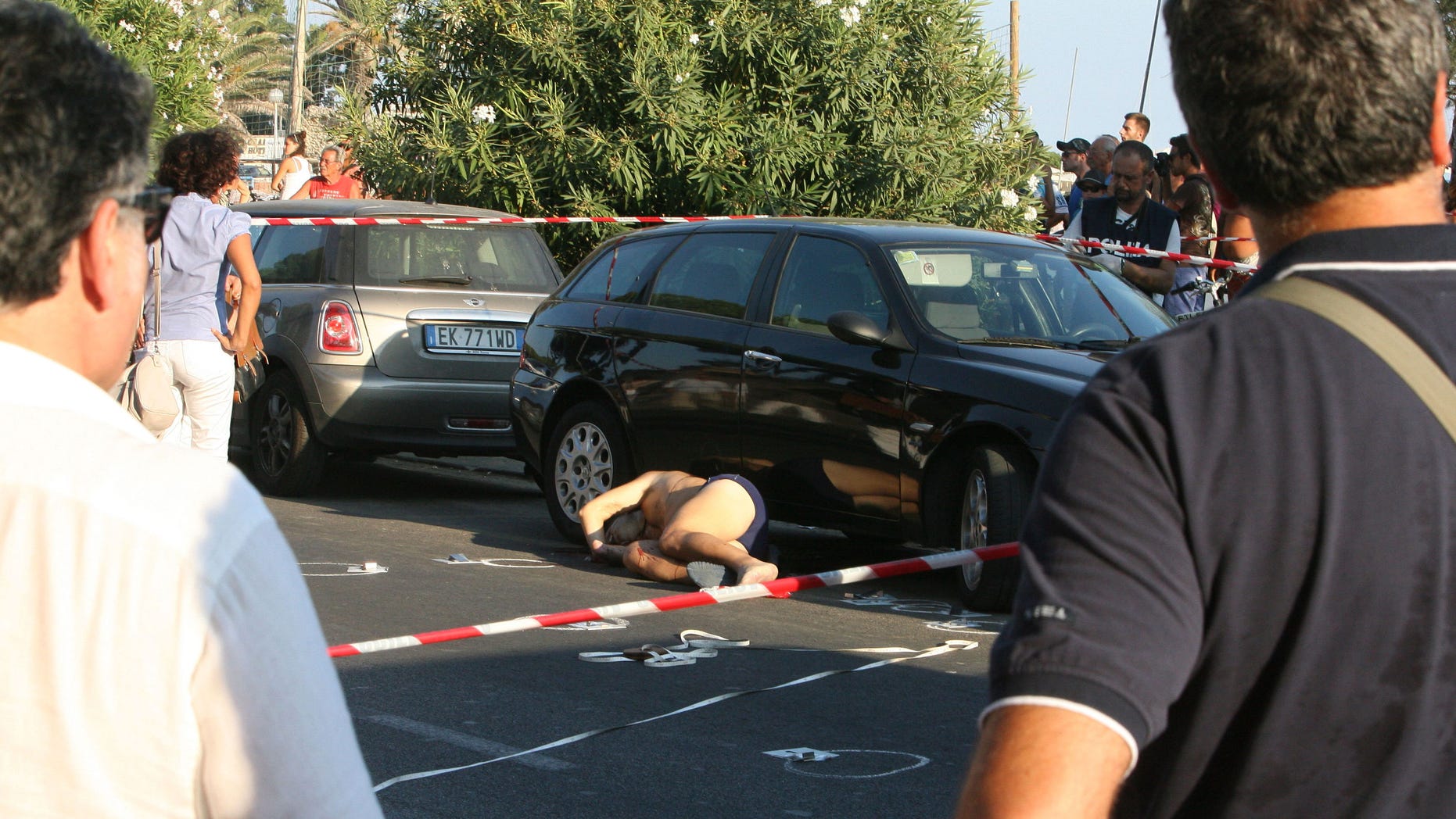 EDS NOTE: GRAPHIC CONTENT - In this photo taken Thursday, Aug. 23, 2012, the dead body of an Italian organized crime boss, Gaetano Marino, center, lies near a car in Terracina, central Italy. Authorities are searching for two men who shot and killed Marino who was vacationing on a beach with his family south of Rome. Police say Gaetano Marino a boss from the Neapolitan Camorra was hit by at least four shots to the head and another five or six to his back Thursday afternoon as he left the beach en route to his hotel in Terracina, 100 kilometers (60 miles) south of Rome in Lazio province. (AP Photo/Fabio Pirazzi)