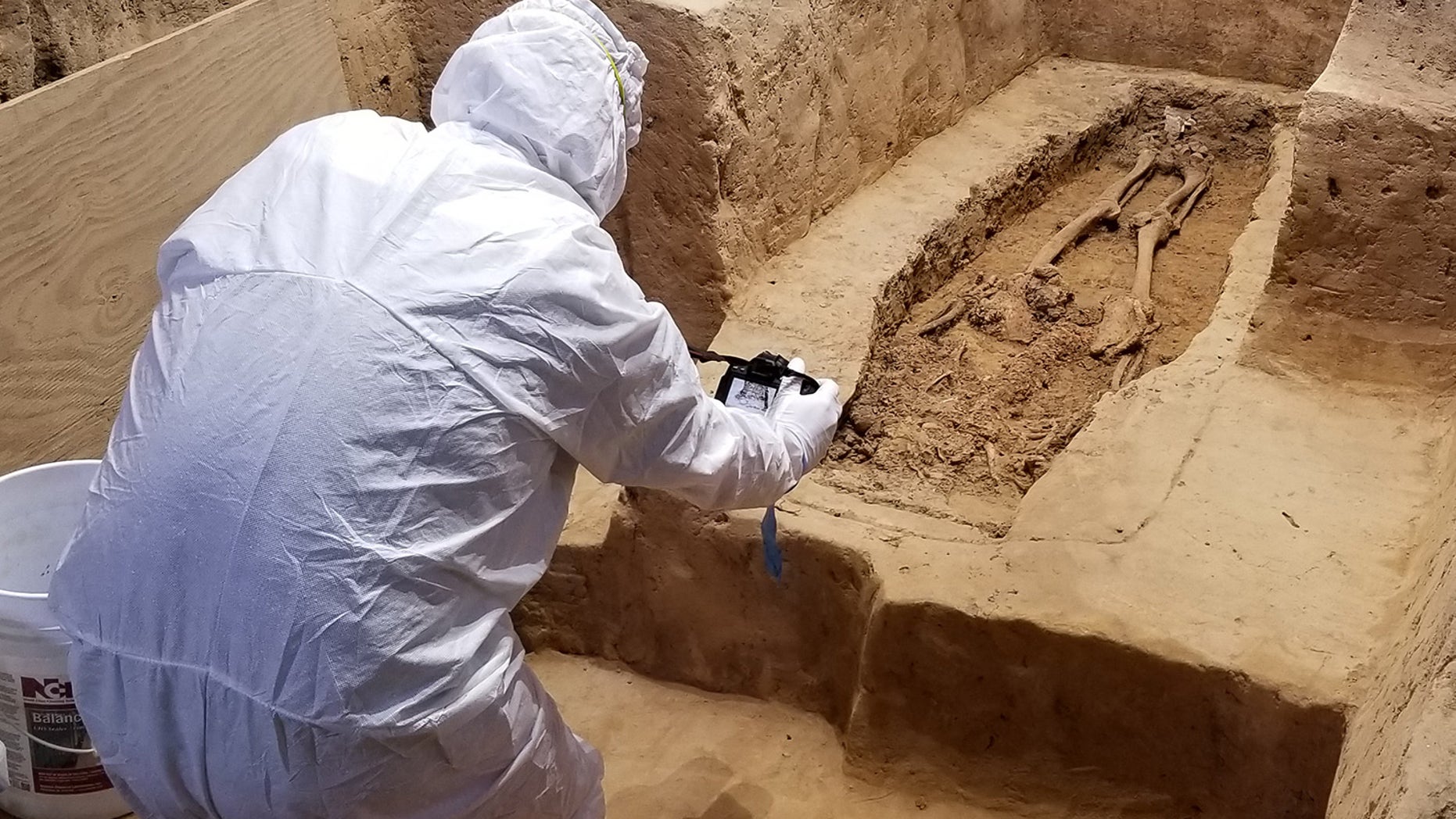 An archaeologist investigates the burial while wearing a suit that will minimize contamination to the historical site.