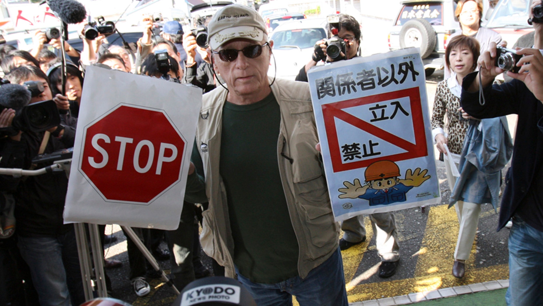 In this Nov. 2, 2010, file photo, Ric O'Barry, a leading global dolphin activist whose efforts to save dolphins is documented in the Oscar-winning film "The Cove," holds "Stop" and "Keep out except persons concerned" signs as he arrives at Taiji Community Center in Taiji, western Japan.