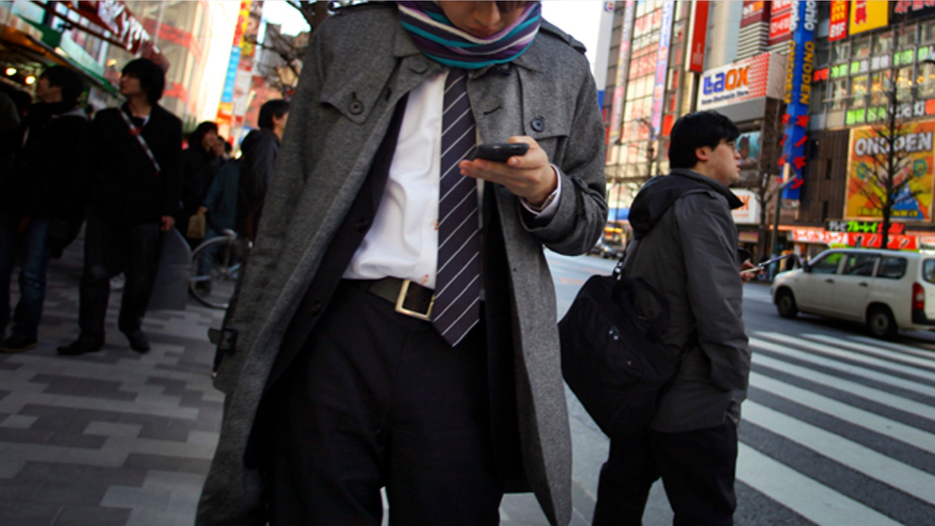 A young man uses a cell phone in a street in Tokyo Friday, March 4, 2011. Japan is engaging in soul-searching after police arrested a 19-year-old accused of cheating on a prestigious university's entrance examination by using his mobile phone to post questions on a popular online forum and get outside help.