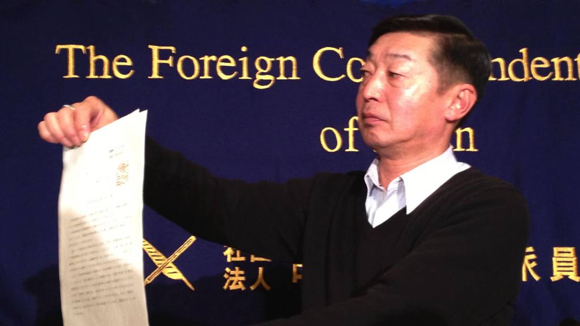 Japanese freelance photographer Yuichi Sugimoto shows the press the original document of an order, signed by Foreign Minister Fumio Kishida, which he was given by Japanese foreign ministry officials at his home, during a news conference in Tokyo Thursday, Feb. 12, 2015. Sugimoto said he was forced to give up his passport because he planned a reporting trip to Syria, which the government has stepped up warnings to its citizens not to visit after two Japanese were killed there in a recent hostage crisis. (AP Photo/Mari Yamaguchi)
