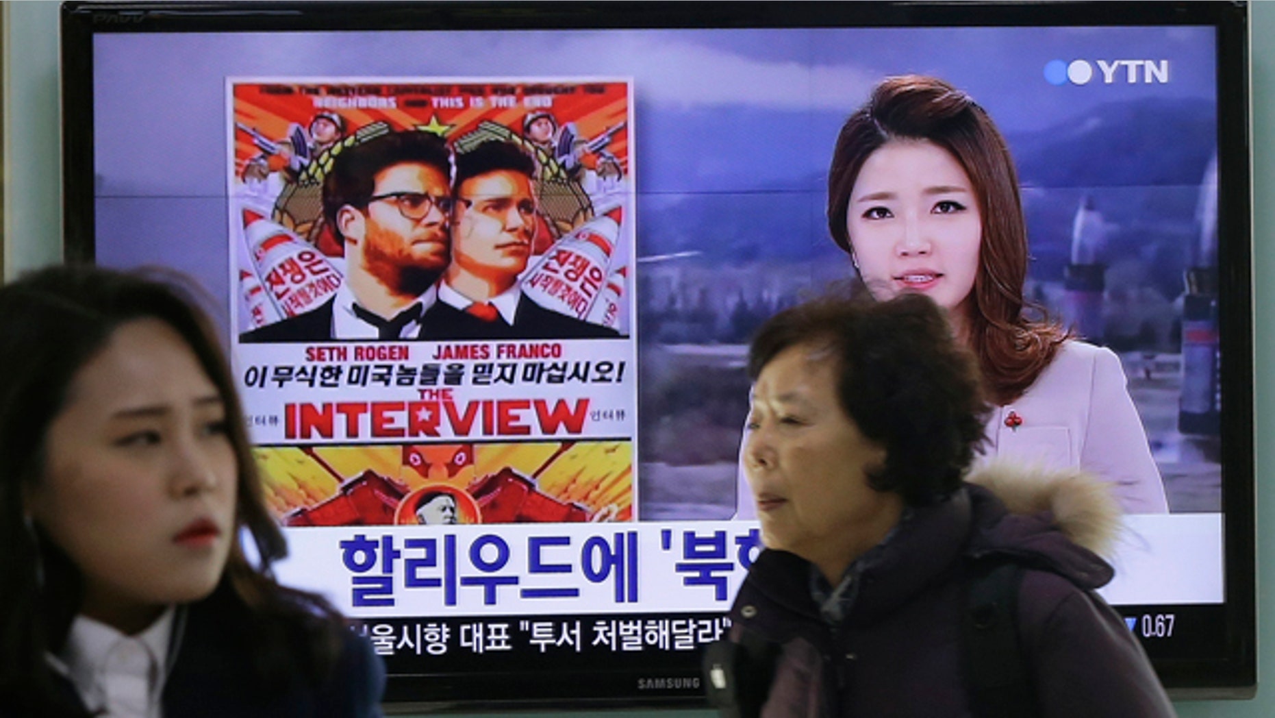 FILE - In this Dec. 22, 2014 file photo, people walk past a TV screen showing a poster of Sony Pictures Entertainment's 'The Interview' in a news report at the Seoul Railway Station in Seoul, South Korea. (AP Photo/Ahn Young-joon, File)