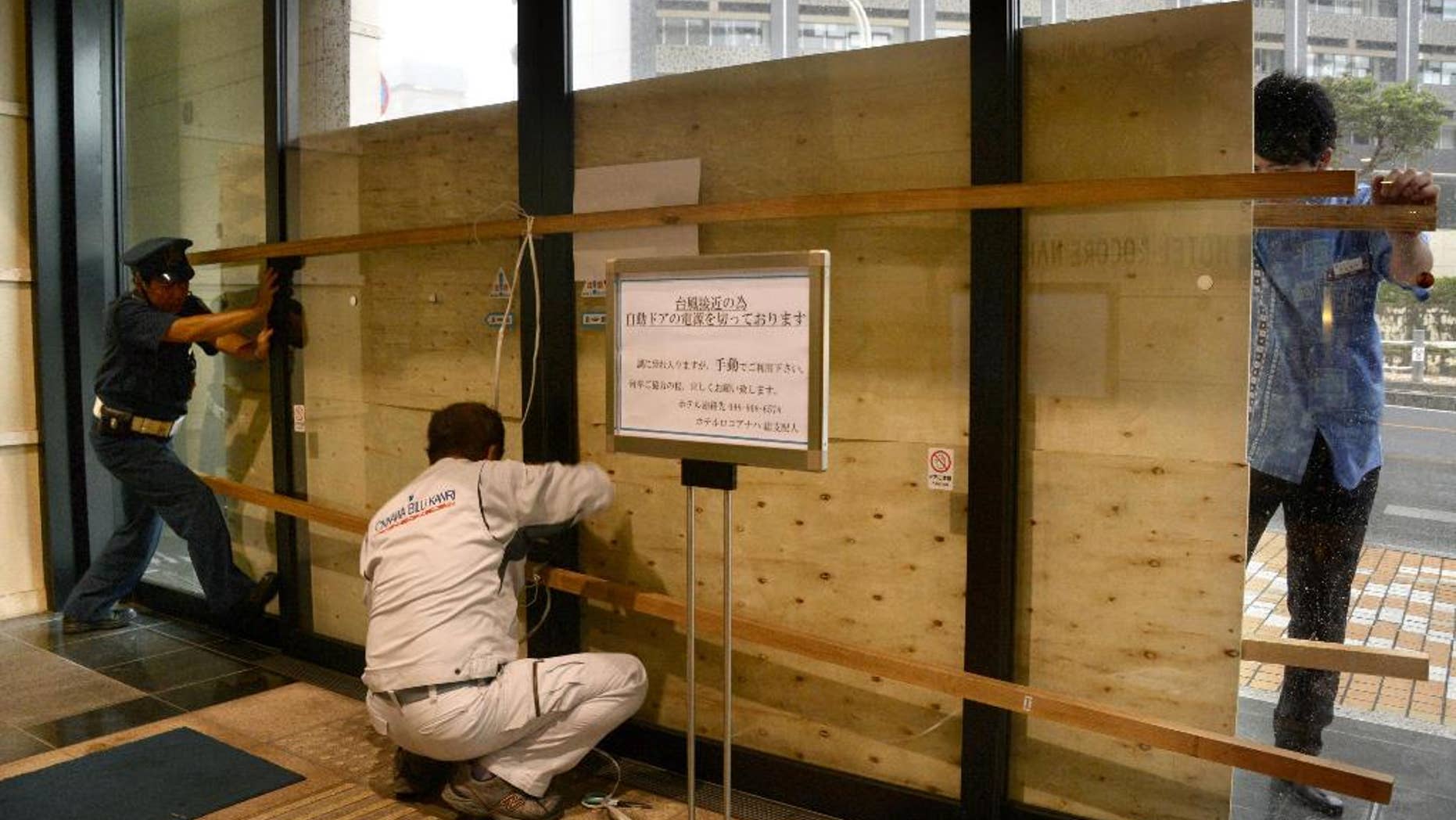 Hotel employees and a guard secure its entrance door with a plywood board in preparation for approaching typhoon Vongfong in Naha, Okinawa, Saturday, Oct. 11, 2014.(AP Photo/Kyodo News) JAPAN OUT, CREDIT MANDATORY