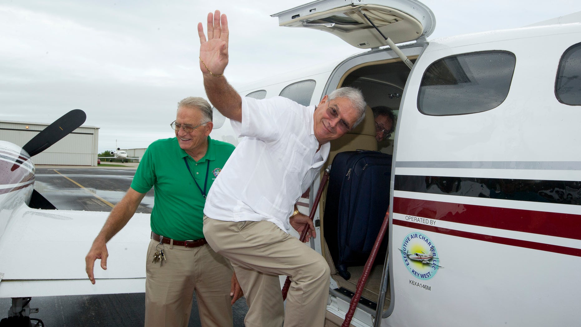 In this photo provided by the Florida Keys News Bureau, Key West Mayor Craig Cates, right, waves goodbye as he boards a chartered aircraft at Key West International Airport Monday, Dec. 30, 2013, that flew to Havana, Cuba. The trip was the first legal commercial passenger flight from Key West to Cuba in more than 50 years and carried passengers who will remain until Jan. 3, 2014. It was organized by the Florida Keys Tropical Research Ecological Exchange Institute under a people-to-people cultural exchange license. Cates accompanied the passengers but did not stay in Cuba and returned to Key West. At left is Monroe County Airports Director Peter Horton. (AP Photo/Florida Keys News Bureau)