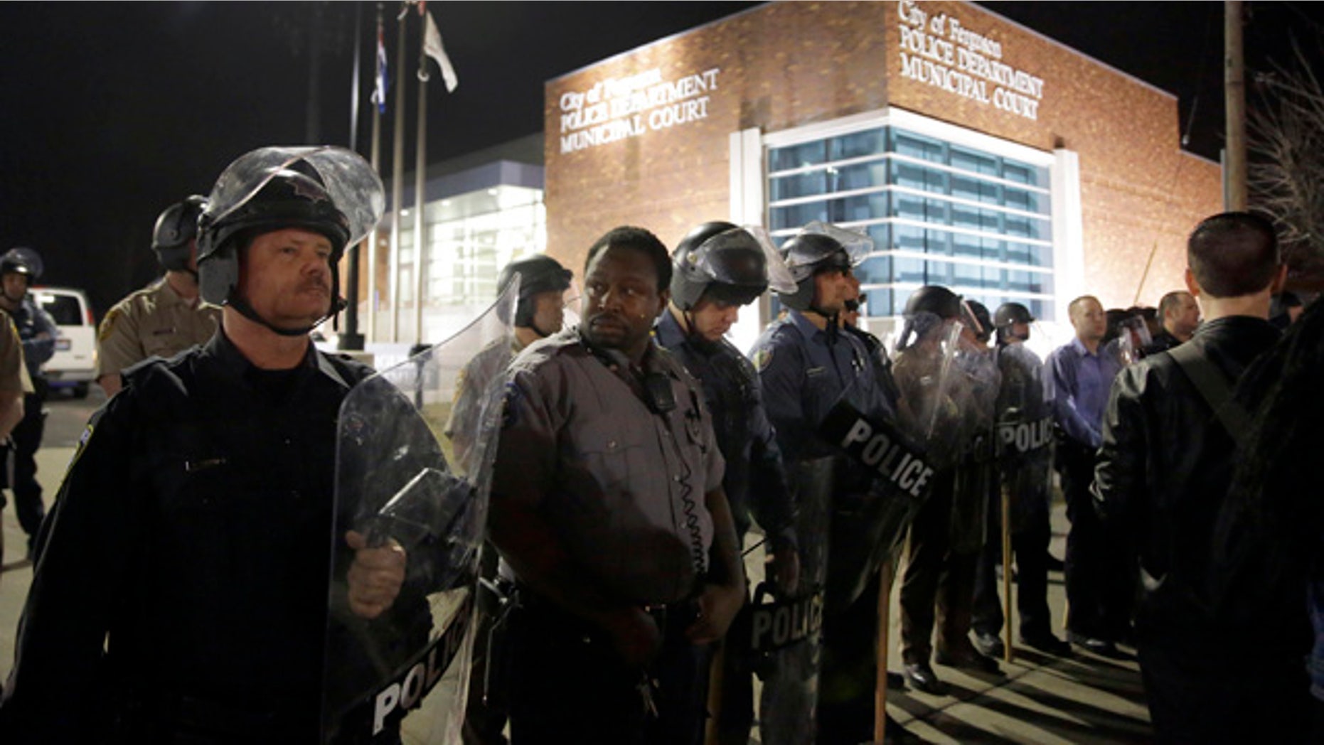 Police form a line outside the Ferguson Police Department as people demonstrate nearby Wednesday, March 11, 2015, in Ferguson, Mo. Earlier in the day, the resignation of Ferguson police chief Thomas Jackson was announced in the wake of a scathing Justice Department report prompted by the fatal shooting of an unarmed black 18-year-old by a white police officer. (AP Photo/Jeff Roberson)