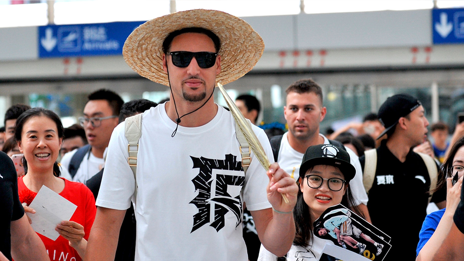 Klay Thompson, with a straw hat on the head, incites a palm-leaf fan as he arrives at the Beijing Capital International Airport in Beijing.
