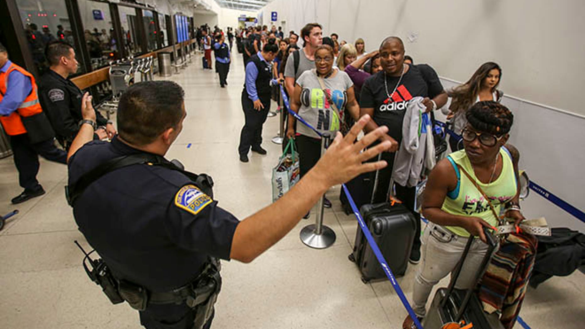 Police officers stand guard as passengers wait in line at Terminal 7 in Los Angeles International Airport, Sunday, Aug. 28, 2016.