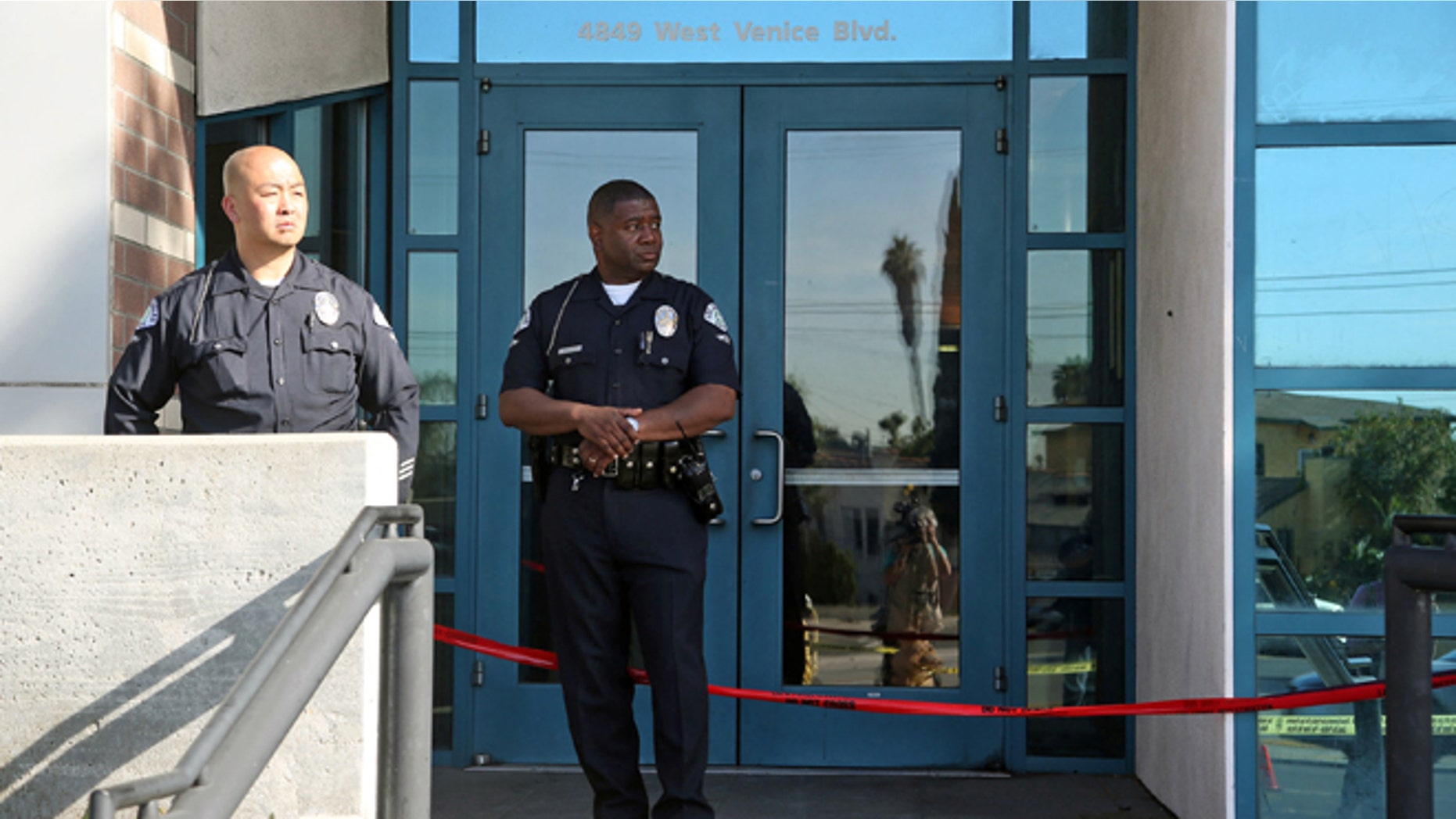 Los Angeles police officers stand outside the West Traffic Division station Tuesday, April 8, 2014, after an officer was shot and wounded inside the station Monday evening. A gunman who opened fire inside the police station, hitting one officer several times, was hospitalized early Tuesday in critical condition after he was wounded in the ensuing gunbattle, authorities said. (AP Photo/Nick Ut )