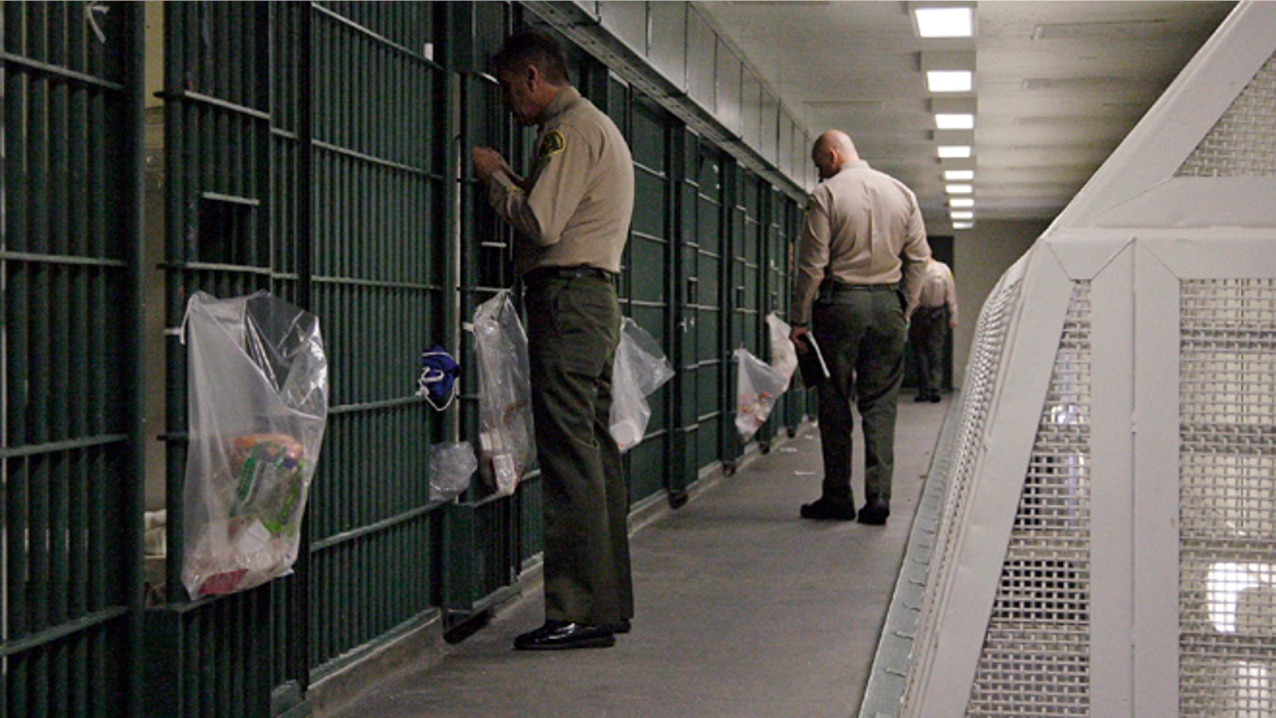 FILE - In this Oct. 3, 2012, file photo, Los Angeles County Sheriff's deputies inspect a cell block at the Men's Central Jail in downtown Los Angeles. Federal officials say 18 current and former Los Angeles County sheriff's deputies saw themselves as being "above the law," engaging in corruption and civil rights abuses that included beating inmates and visitors, falsifying reports, and trying to block an FBI probe of the nation's largest jail system. (AP Photo/Reed Saxon, File)